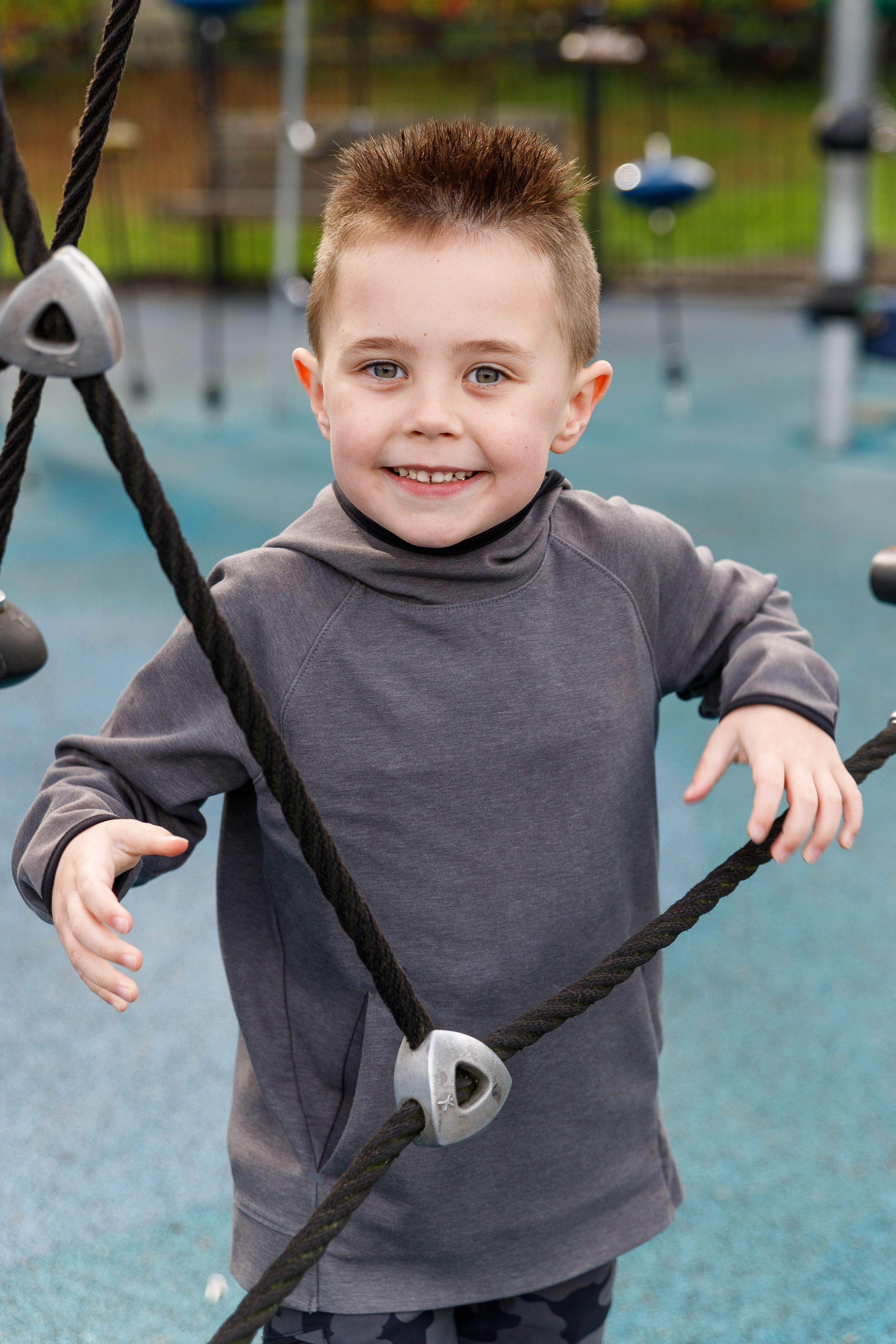 Child playing on playground equipment wearing grey sweatshirt.