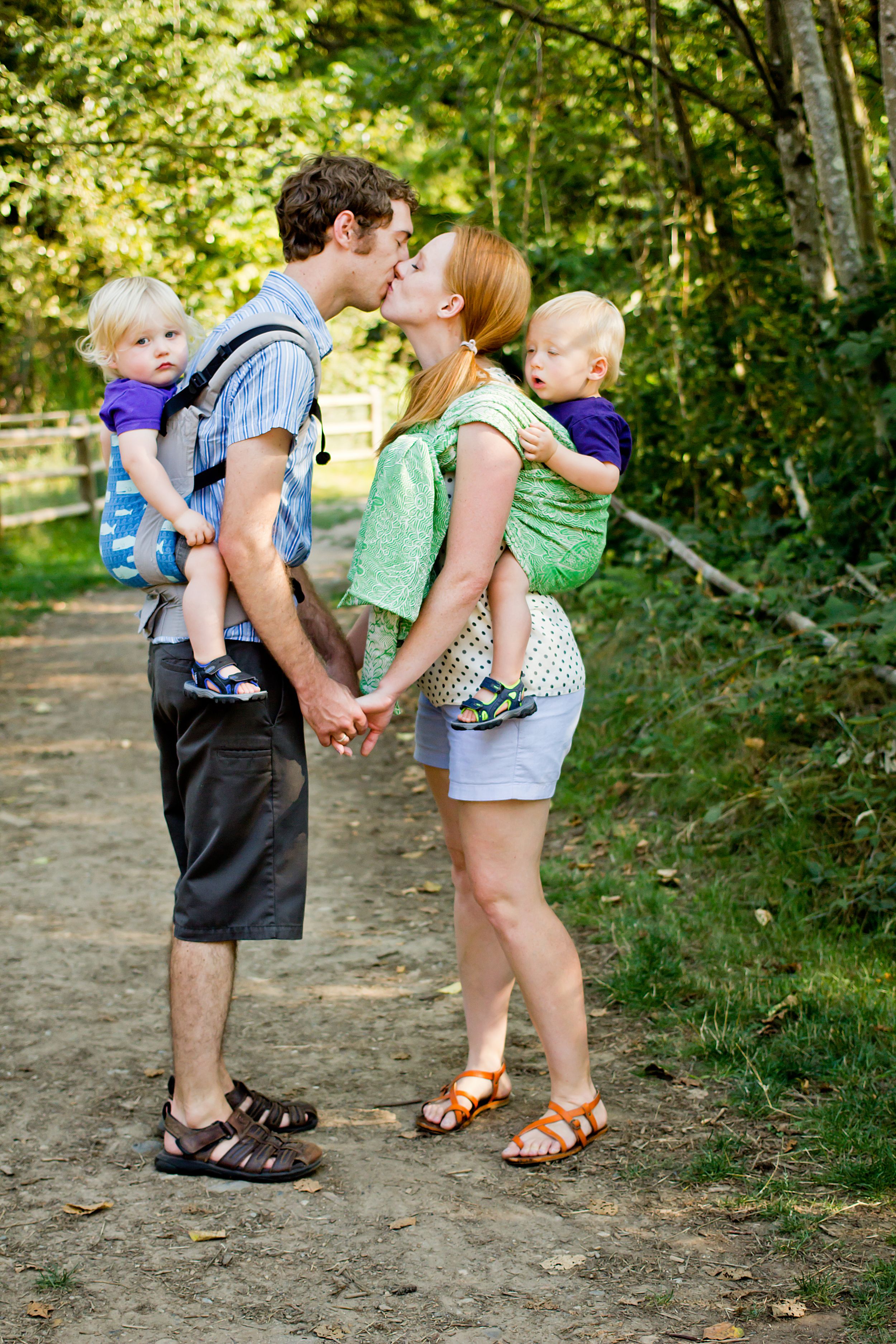 Couple sharing a romantic moment on a forest path while baby wearing.