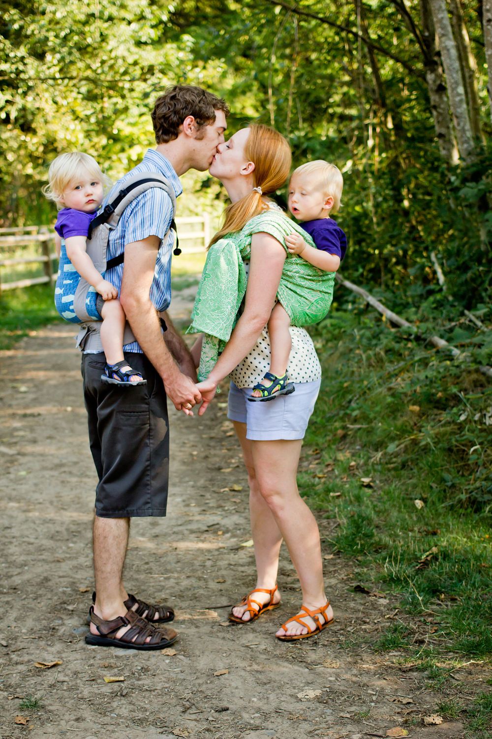Couple sharing a romantic moment on a forest path while baby wearing.