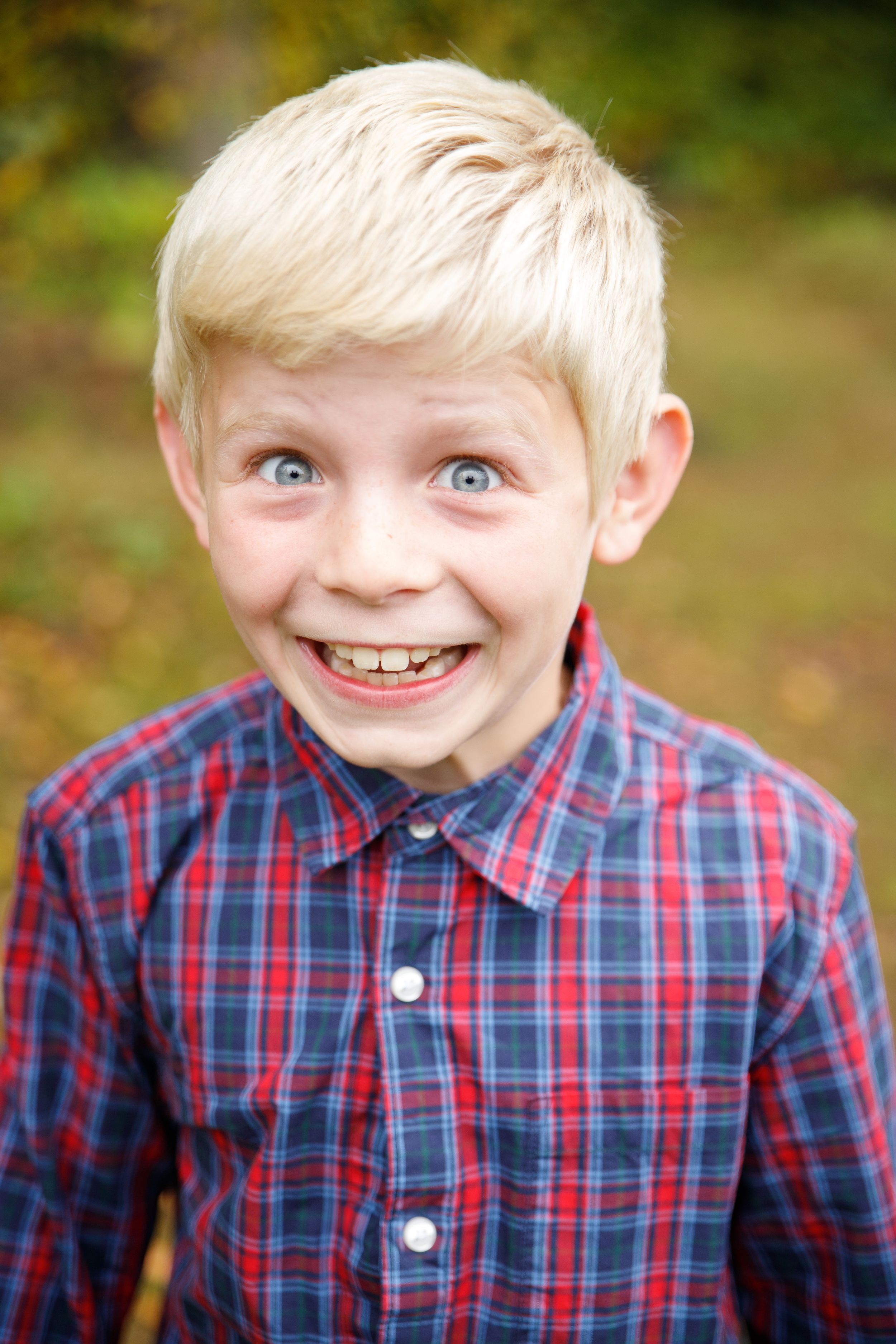 Young child in plaid shirt smiling outdoors during fall season.