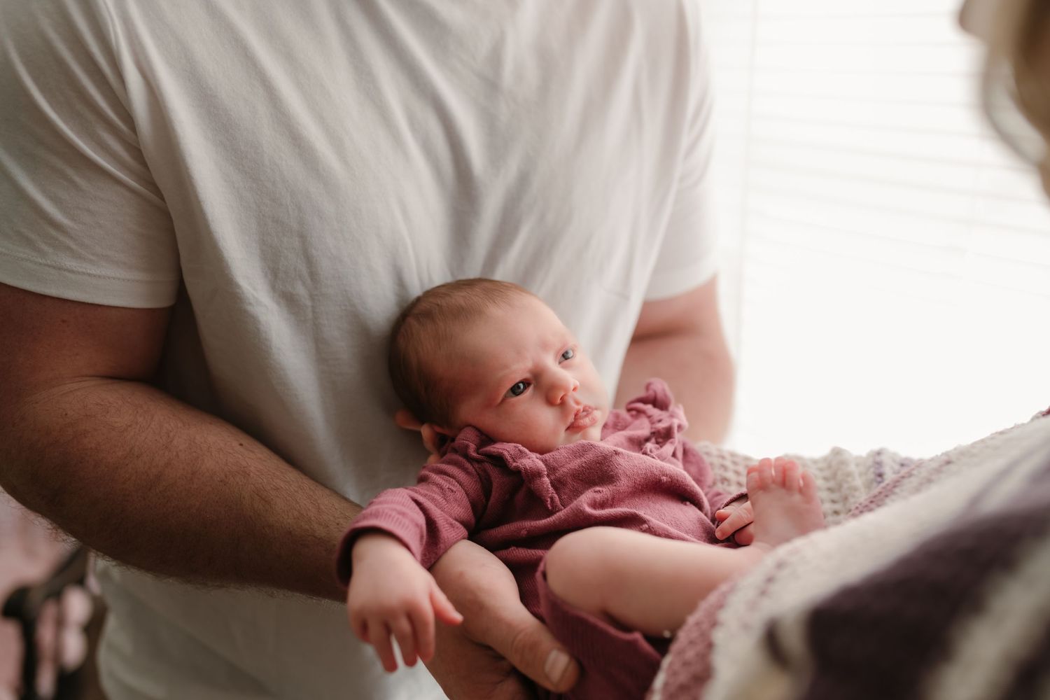 A newborn baby wearing a pink outfit rests peacefully against someone in a white shirt.