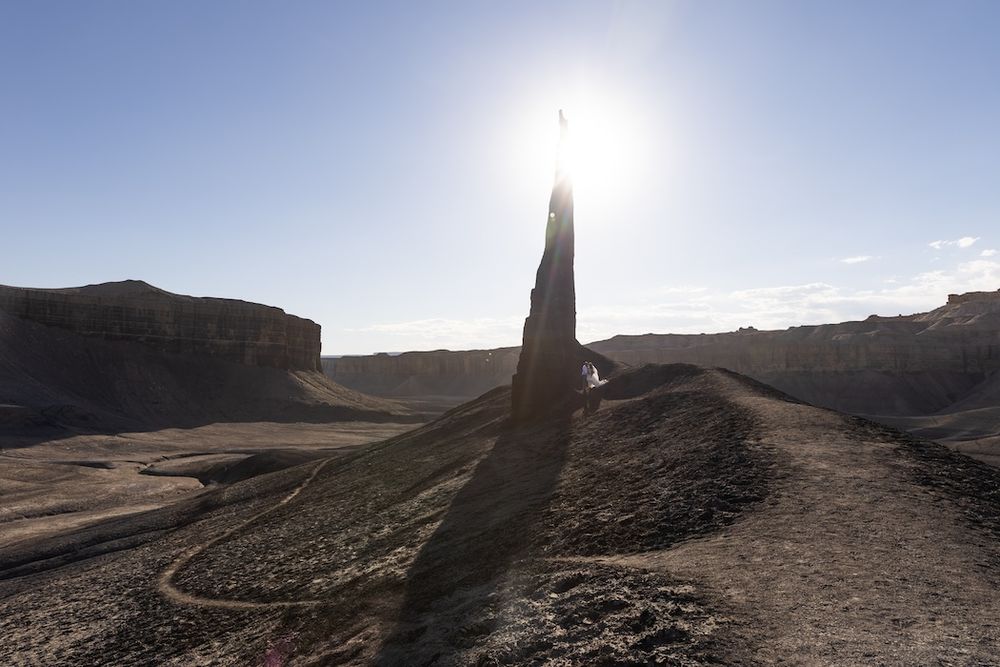 Scenic panoramic view of rugged desert canyons and rock formations under a bright blue sky at sunset.