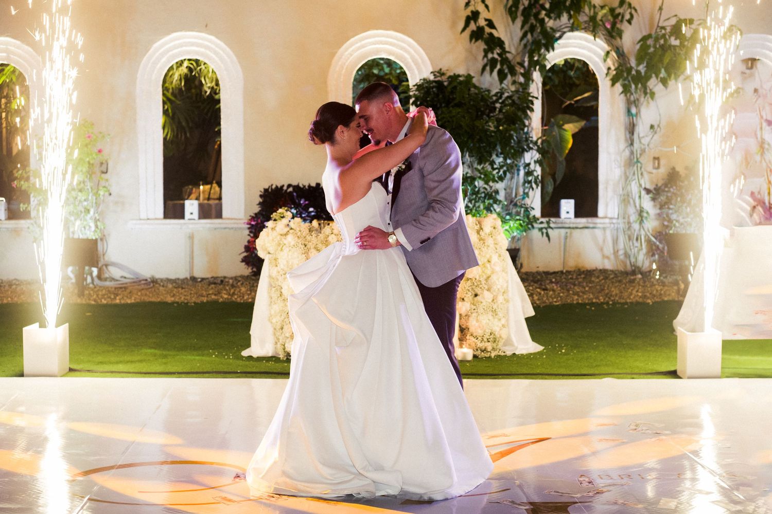 A romantic first dance moment with sparklers and arched windows in an elegant venue.