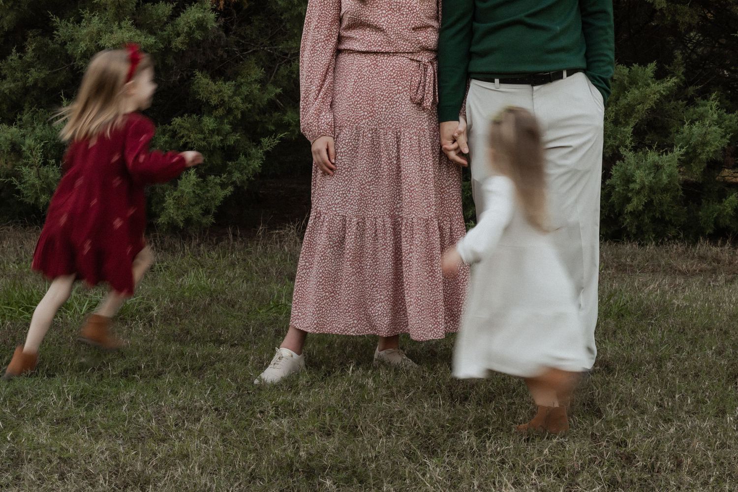 Motion blur captures children and adults playing in a grassy field, with flowing dresses in burgundy, pink and white colors.