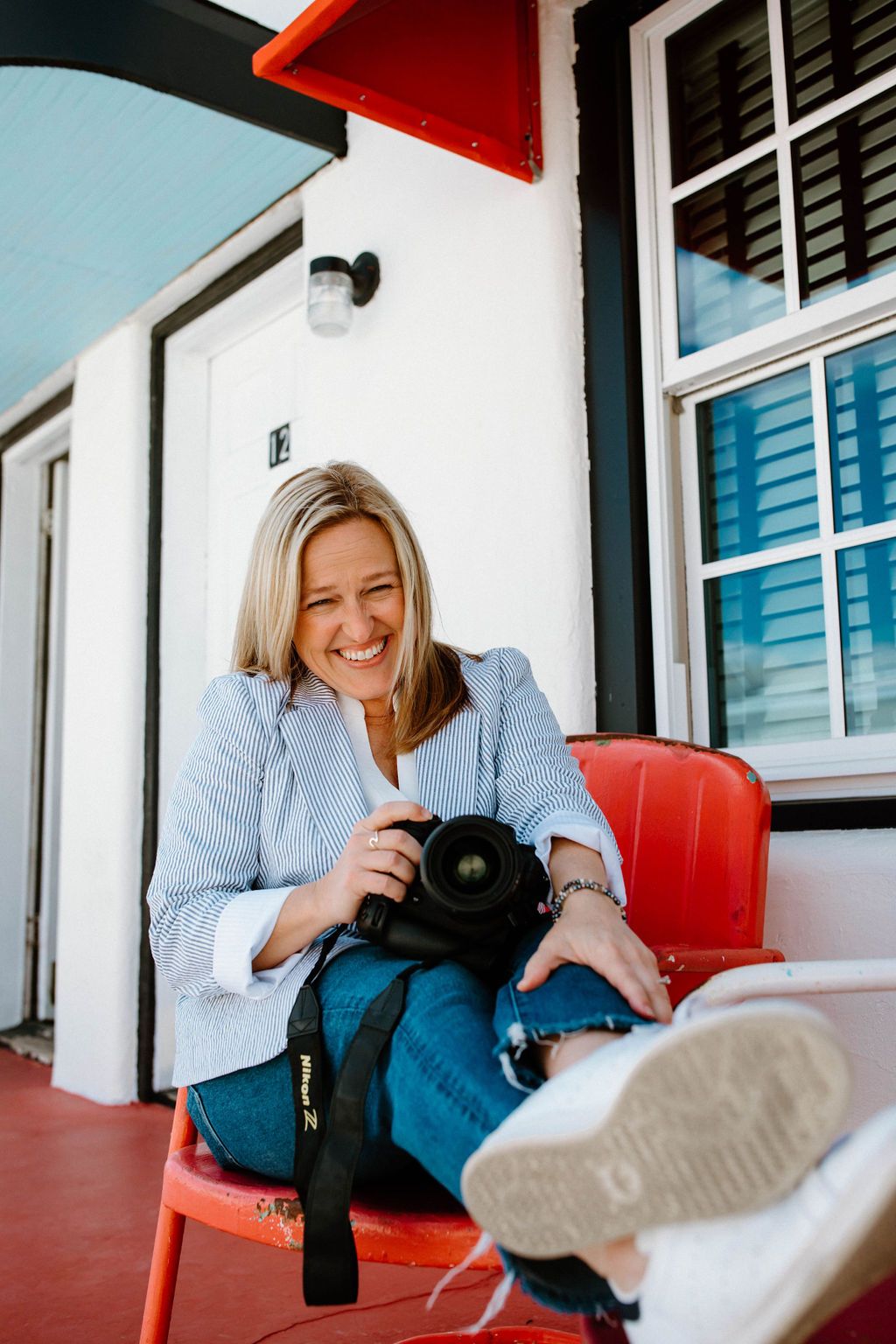 Photographer sitting in red chair reviewing images on camera with relaxed posture.