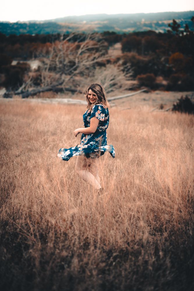 A person in a blue floral dress appears to be floating or jumping in a golden meadow at sunset.