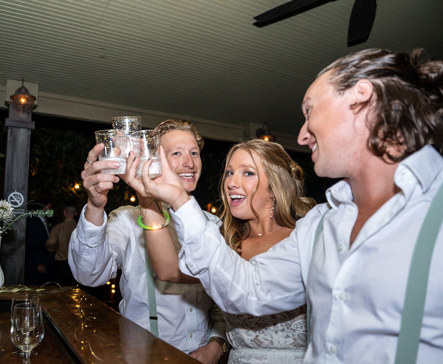 Wedding guests raise their glasses in celebration at a bar during a reception.