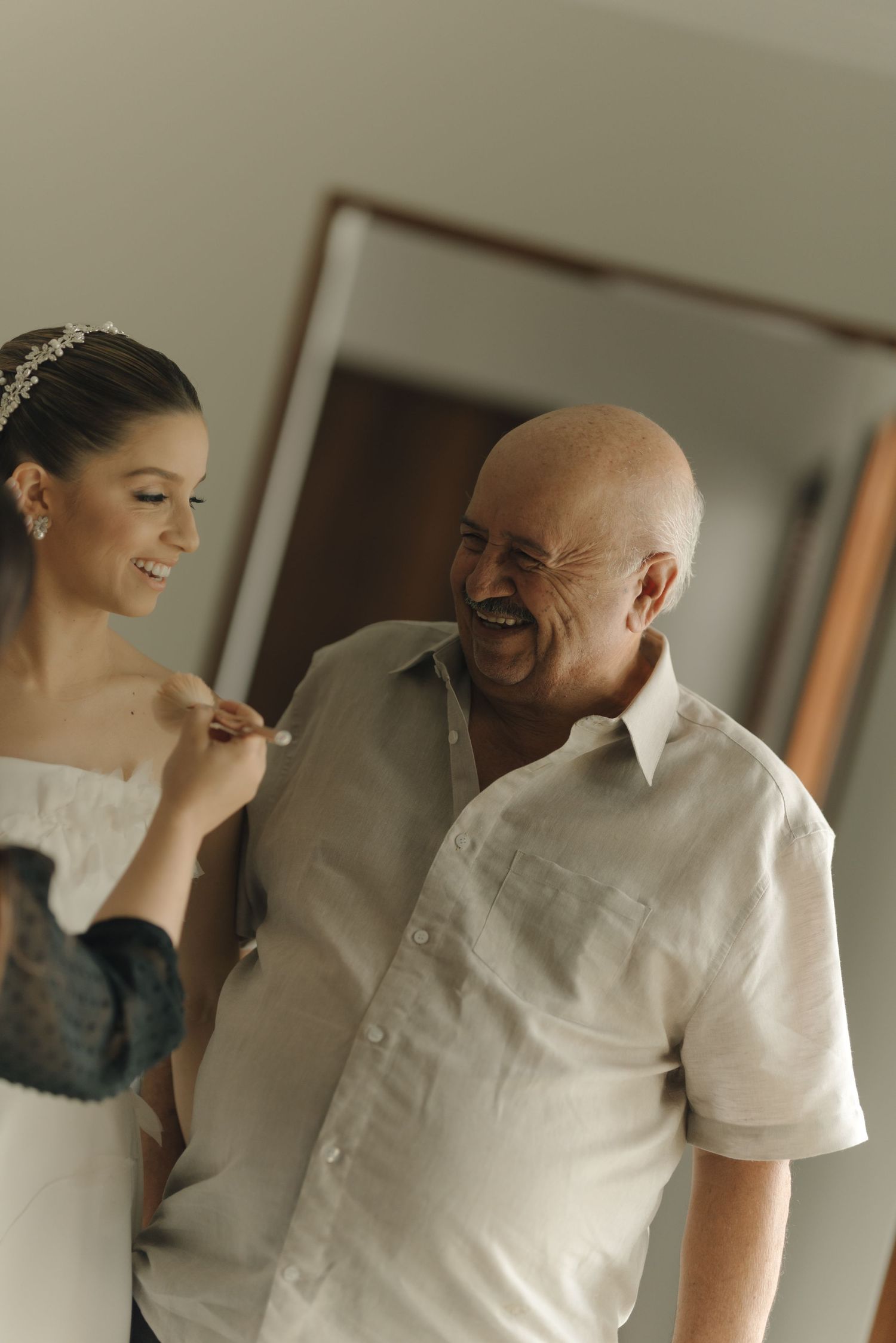 A touching candid moment between a bride in white and an older man sharing a laugh before the wedding ceremony.