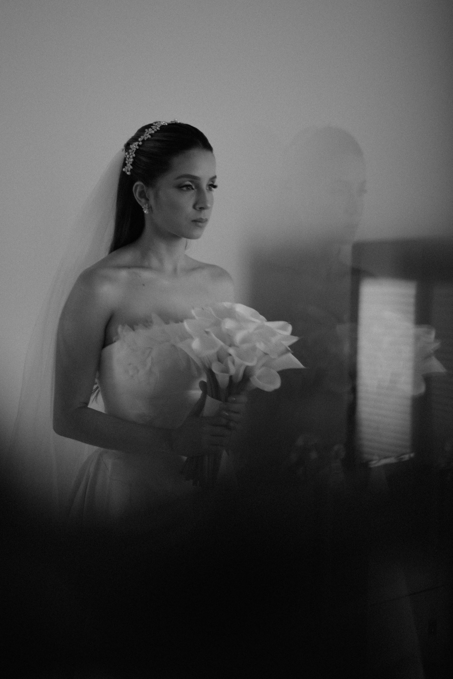 An artistic black and white portrait of a bride holding her bouquet with her reflection visible.