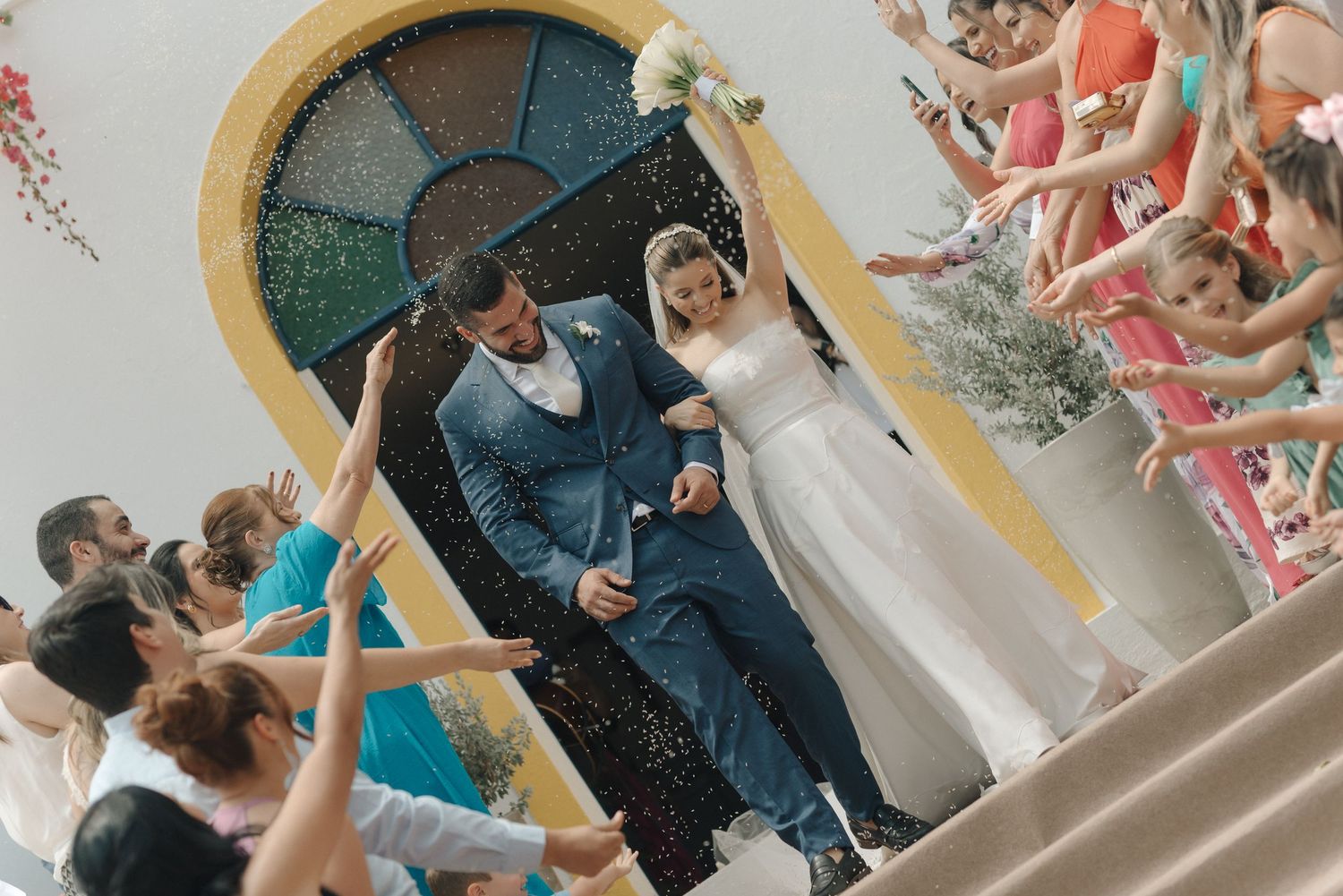 Wedding guests throw confetti as the couple celebrates on the church steps.