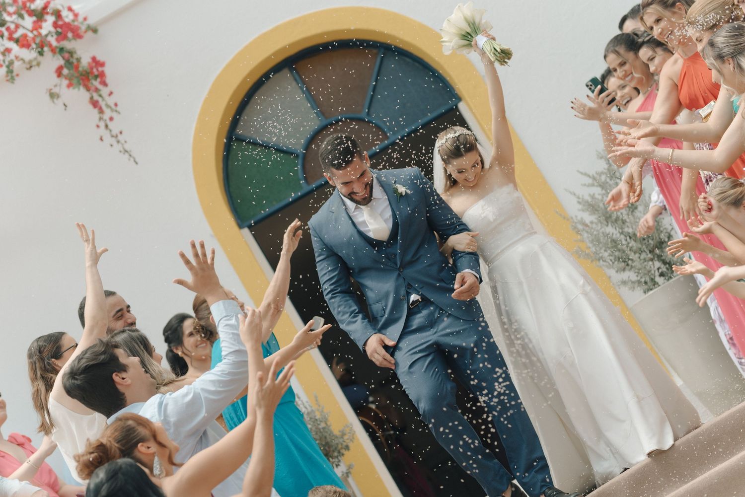 Joyful wedding guests throw confetti at the newly married couple exiting through the church's arched doorway.