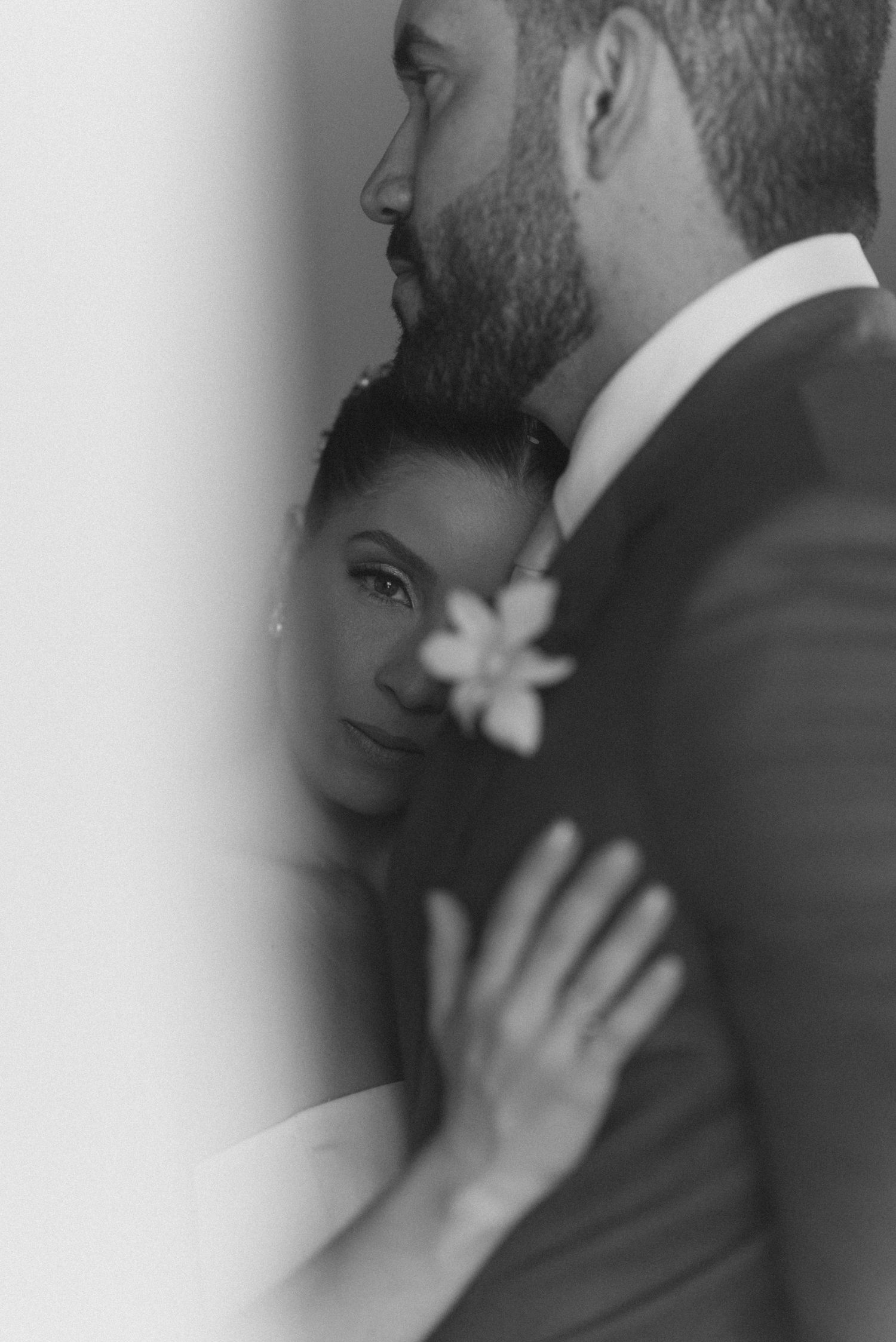 Black and white portrait of newlyweds in a tender moment with floral accessories.