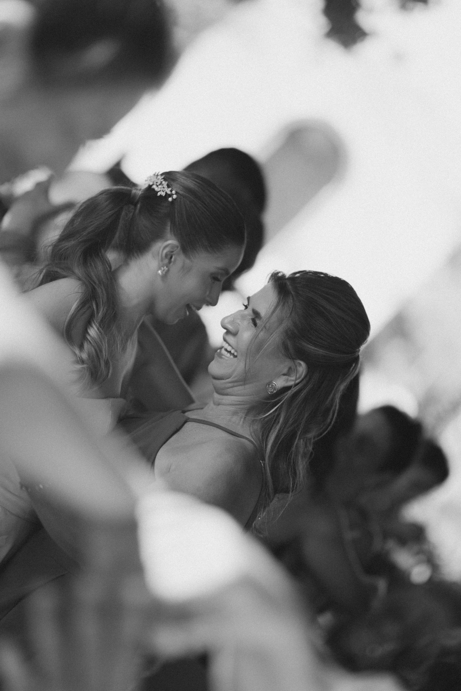 Black and white candid shot of two wedding guests sharing a joyful moment.