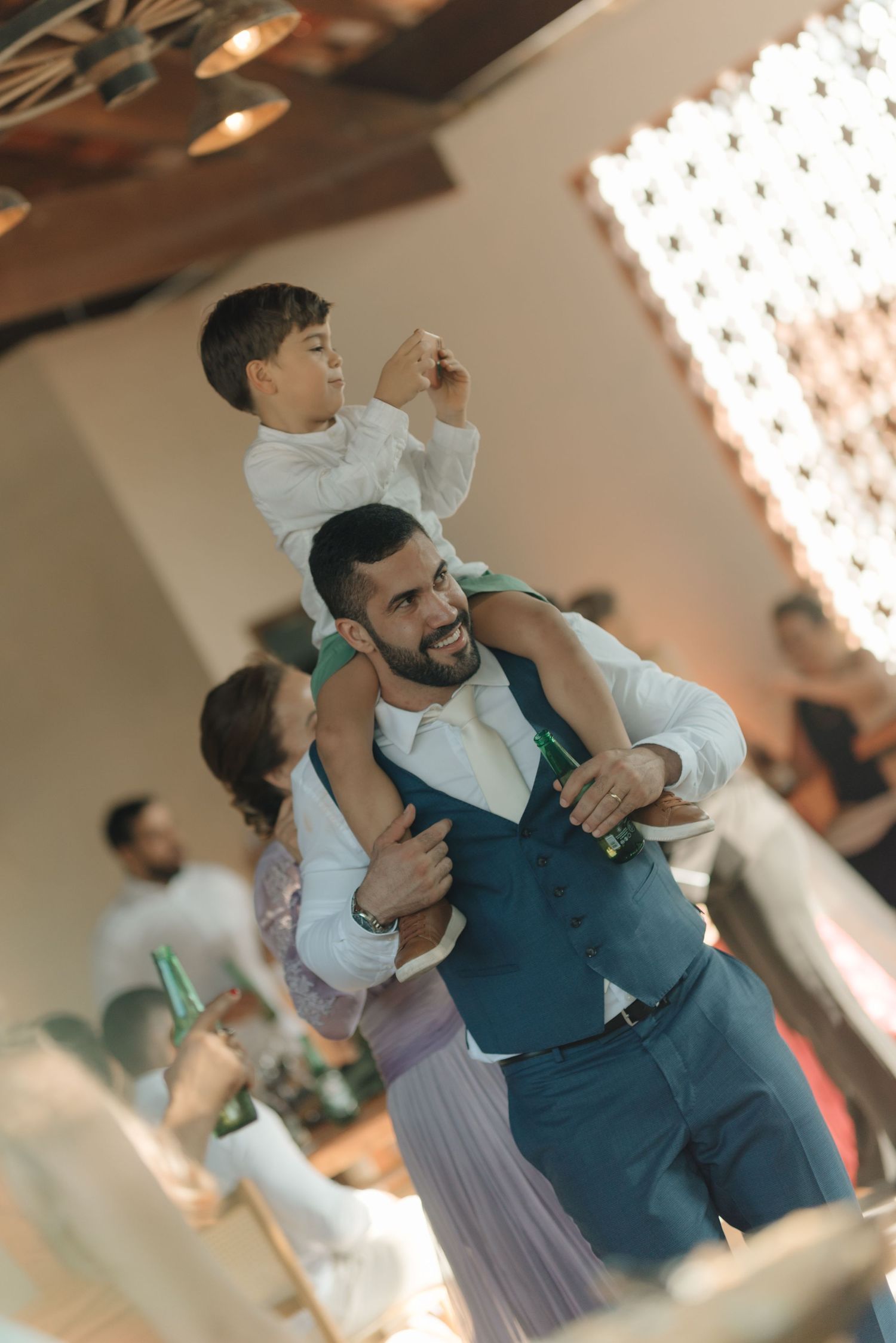 Wedding guest carries child on shoulders during reception celebration.
