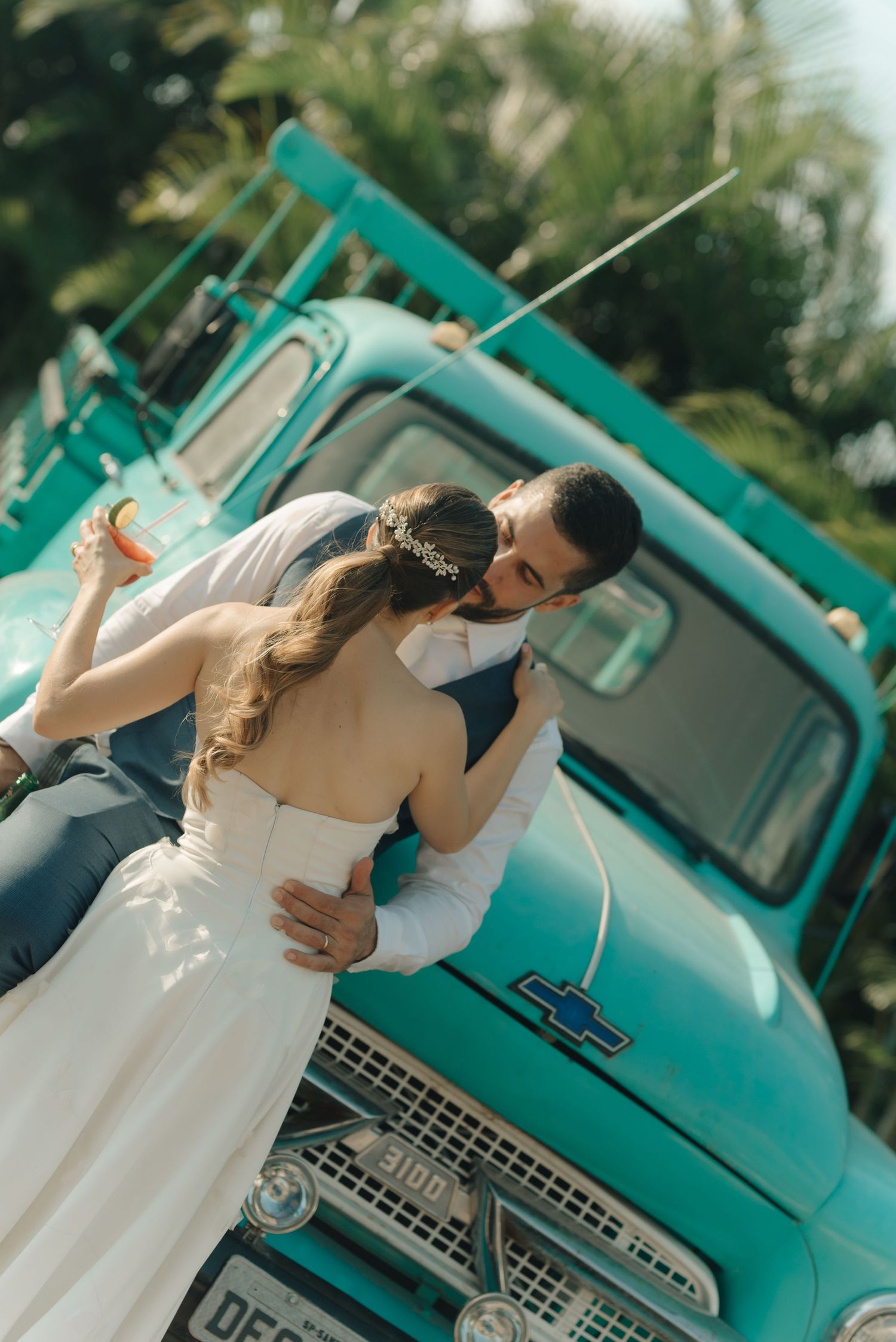 Bride and groom share romantic kiss in front of vintage turquoise truck.