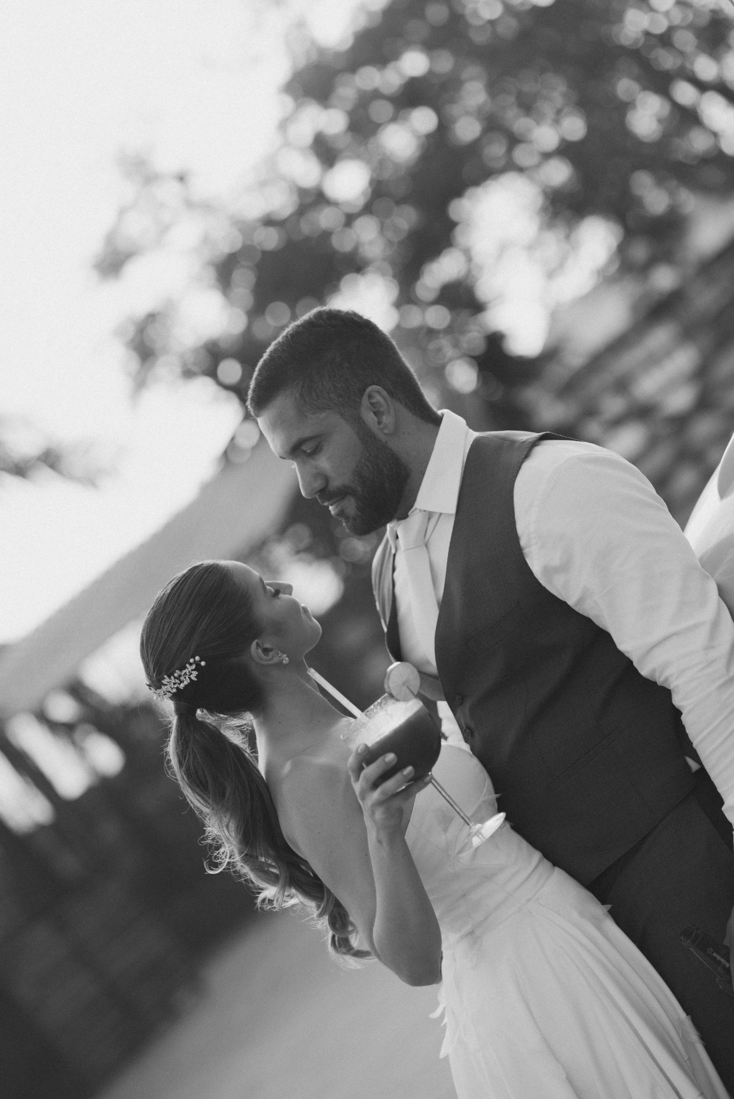 Black and white photo of couple sharing intimate moment by vintage car.