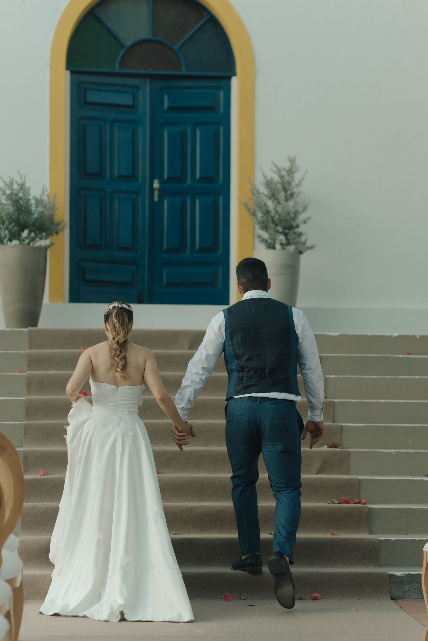 A couple ascending church steps with a distinctive teal door and yellow archway on their wedding day.