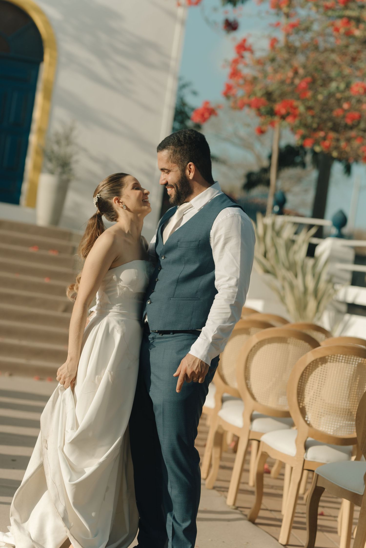 Wedding couple sharing an intimate moment outside a church with red flowers blooming in background.