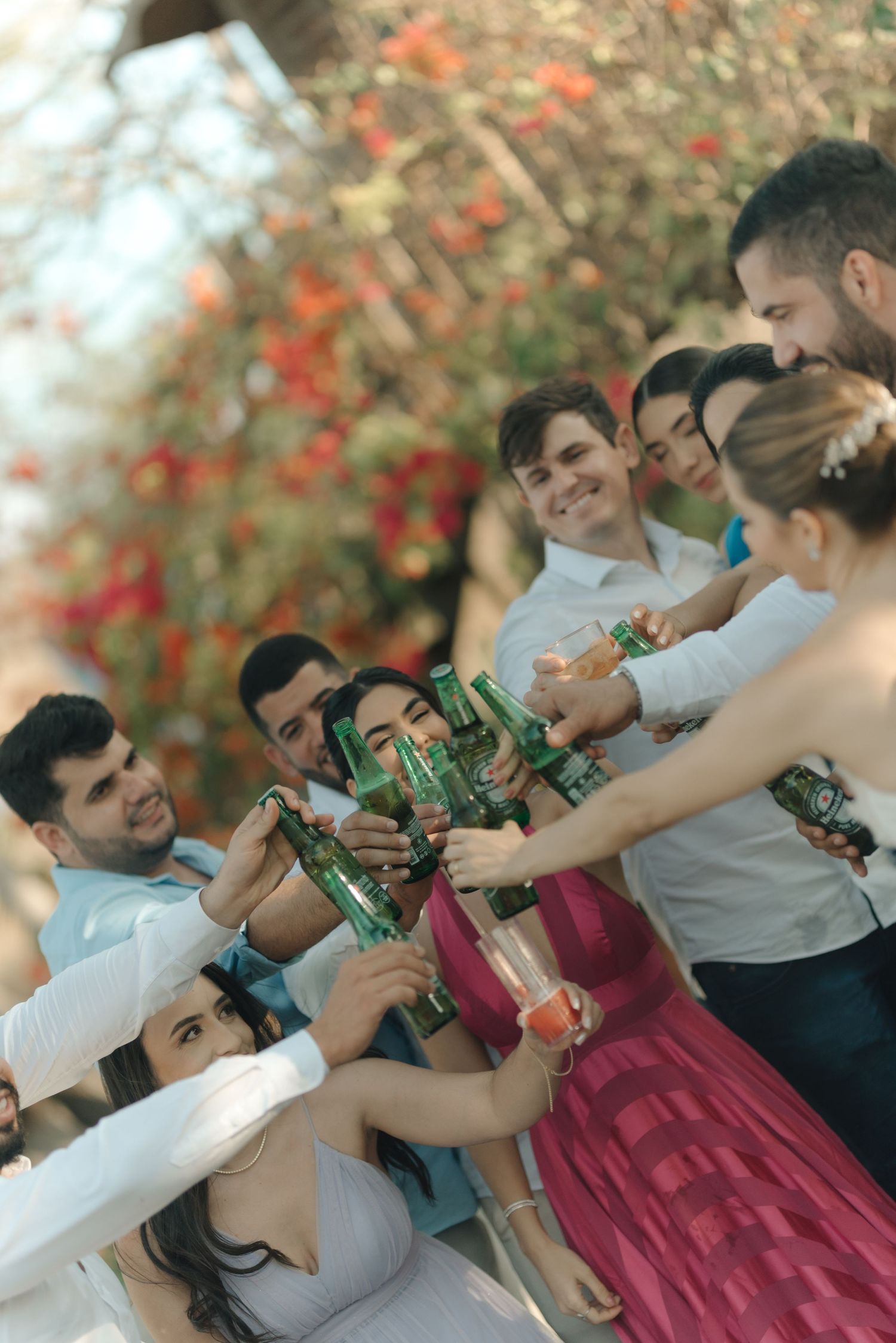 Wedding party toasting with green bottles during outdoor celebration.