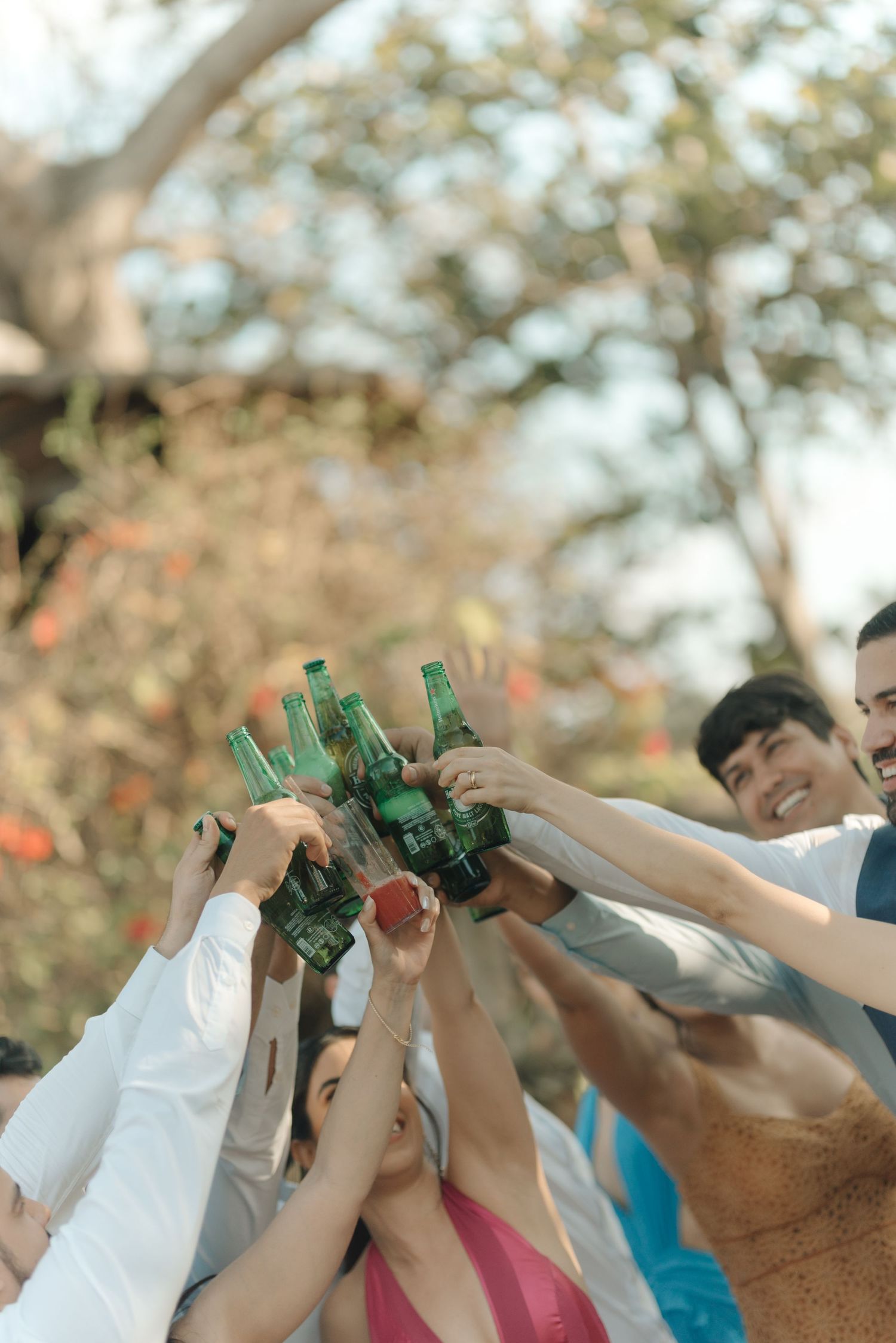 Group raising bottles in celebratory toast during outdoor wedding gathering.