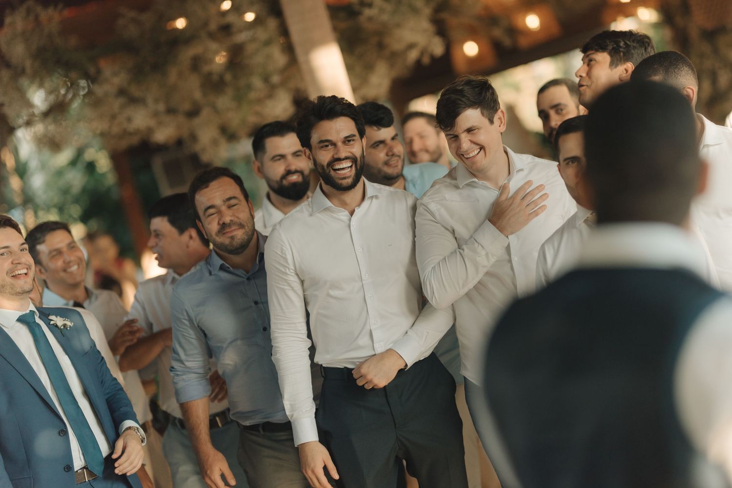 Group of wedding guests gathered outdoors sharing laughs under string lights.