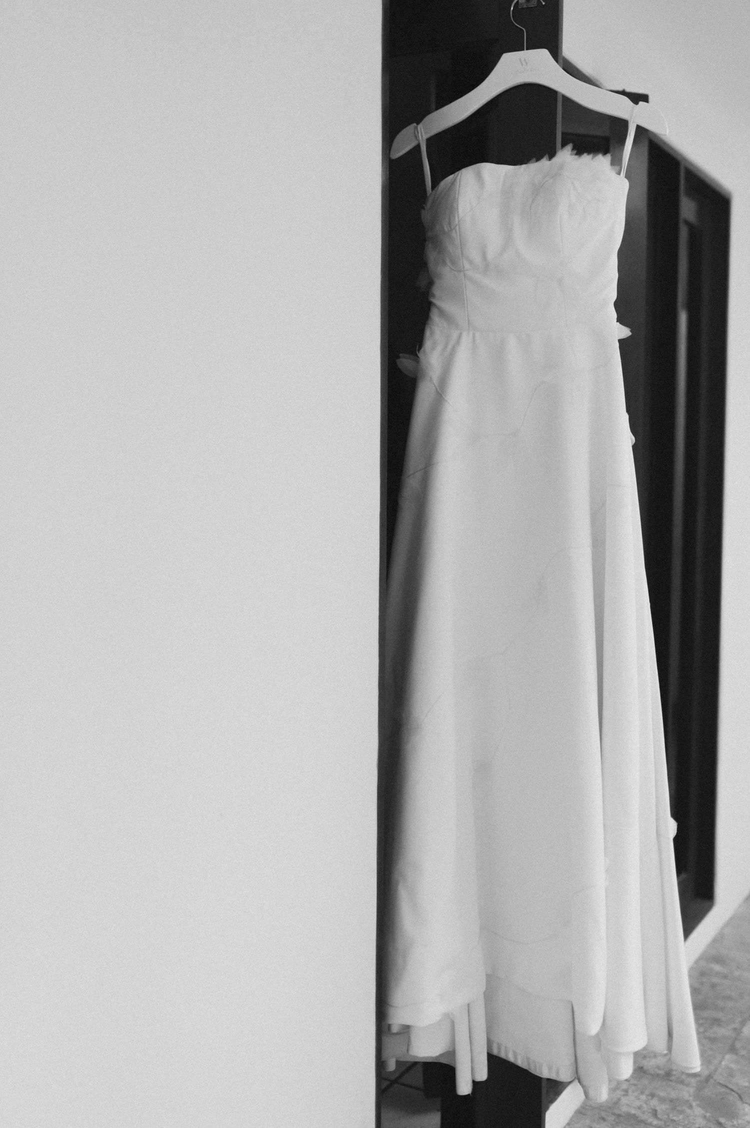 White wedding dress hanging on display against dark wall in black and white photograph.