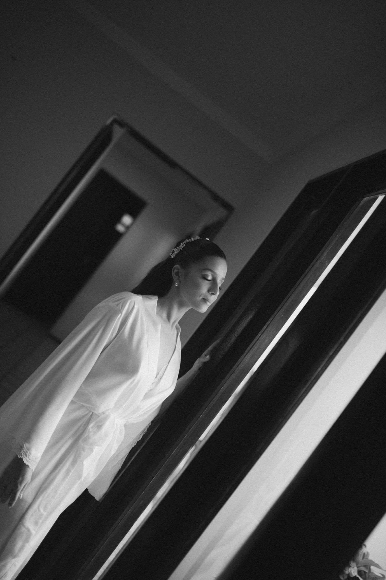 Artistic black and white portrait of person in white robe by window.