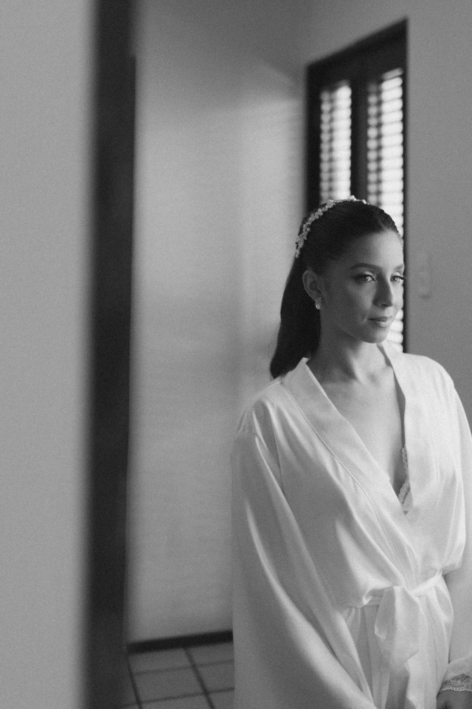 Elegant black and white portrait of person in flowing white robe by window.