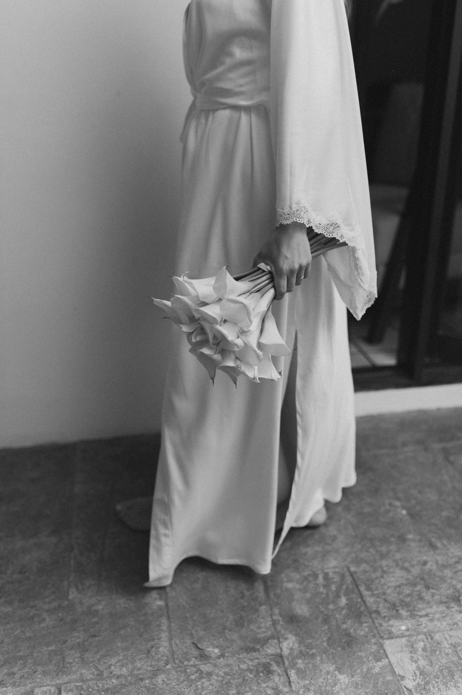 Close-up of a bride's dress hem and bouquet in black and white photography.