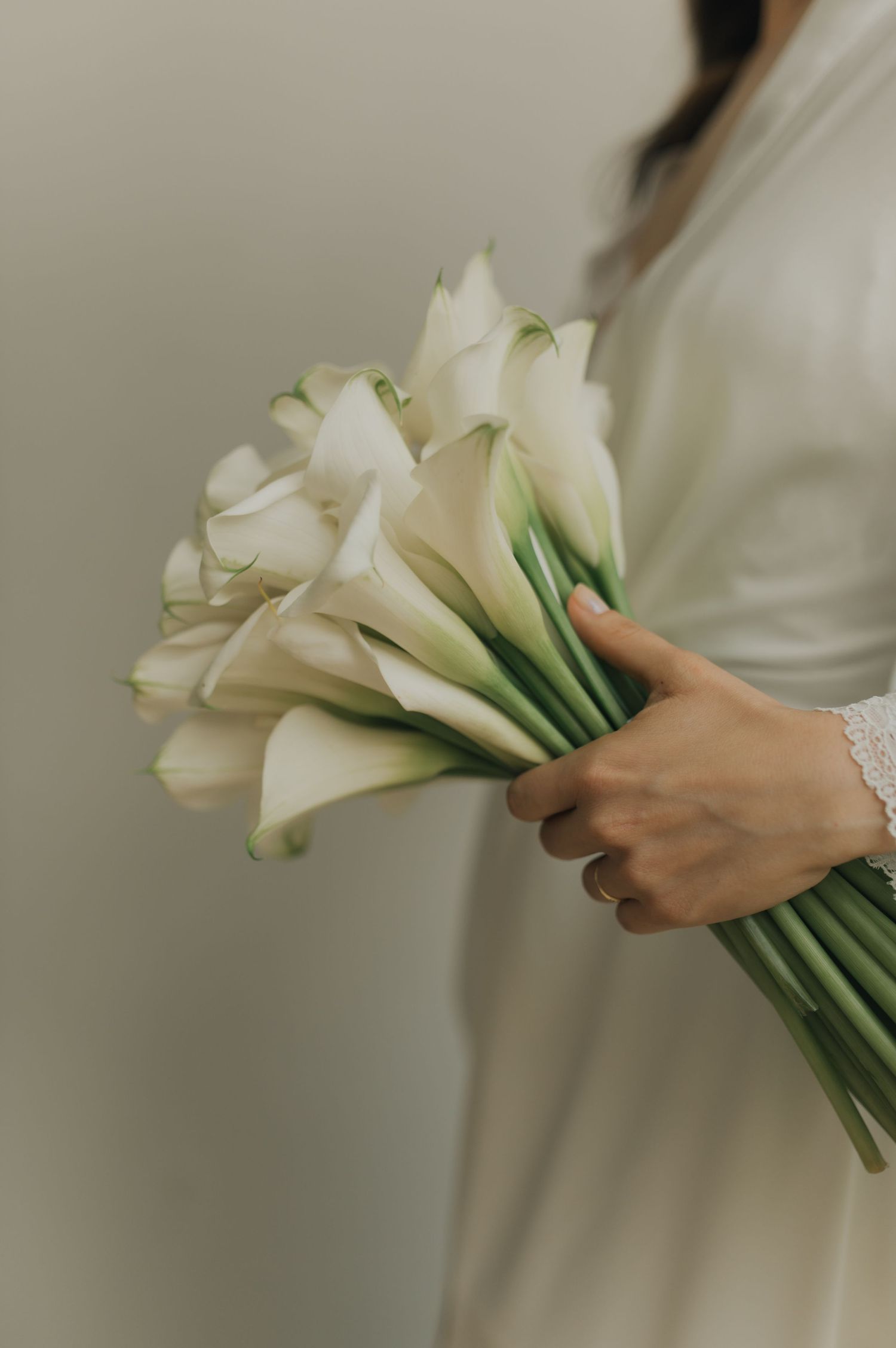 A delicate bouquet of white calla lilies held by hands in a wedding dress.