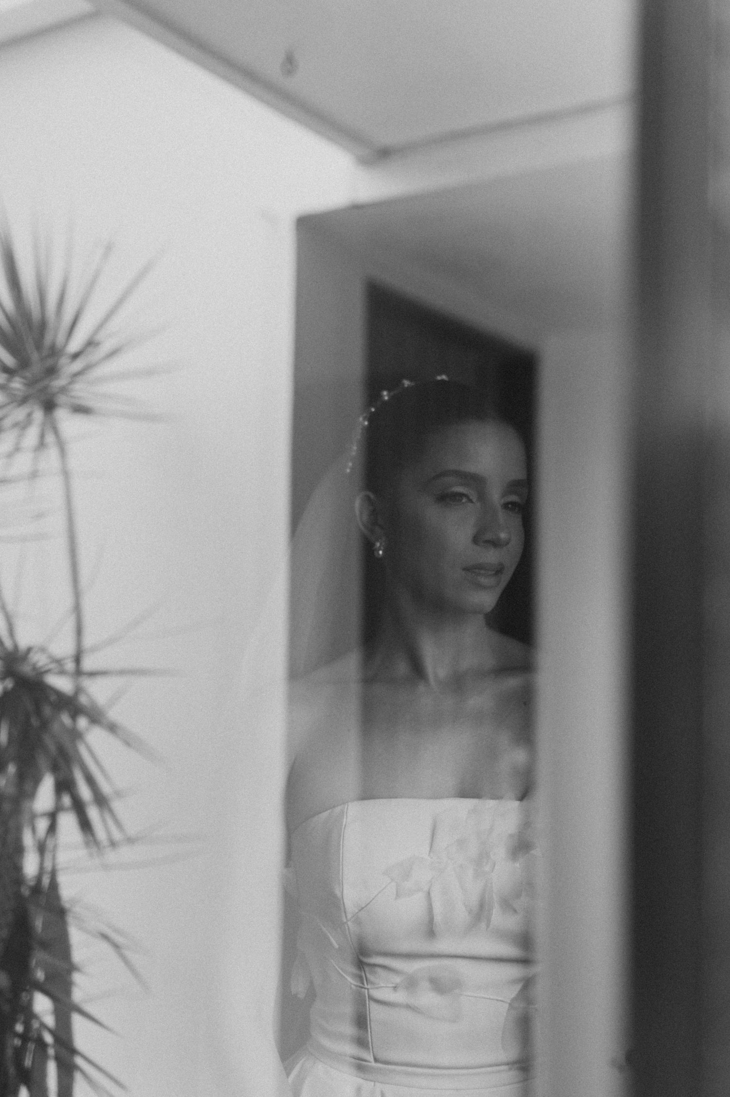 Artistic reflection of a bride in white dress captured through window glass.