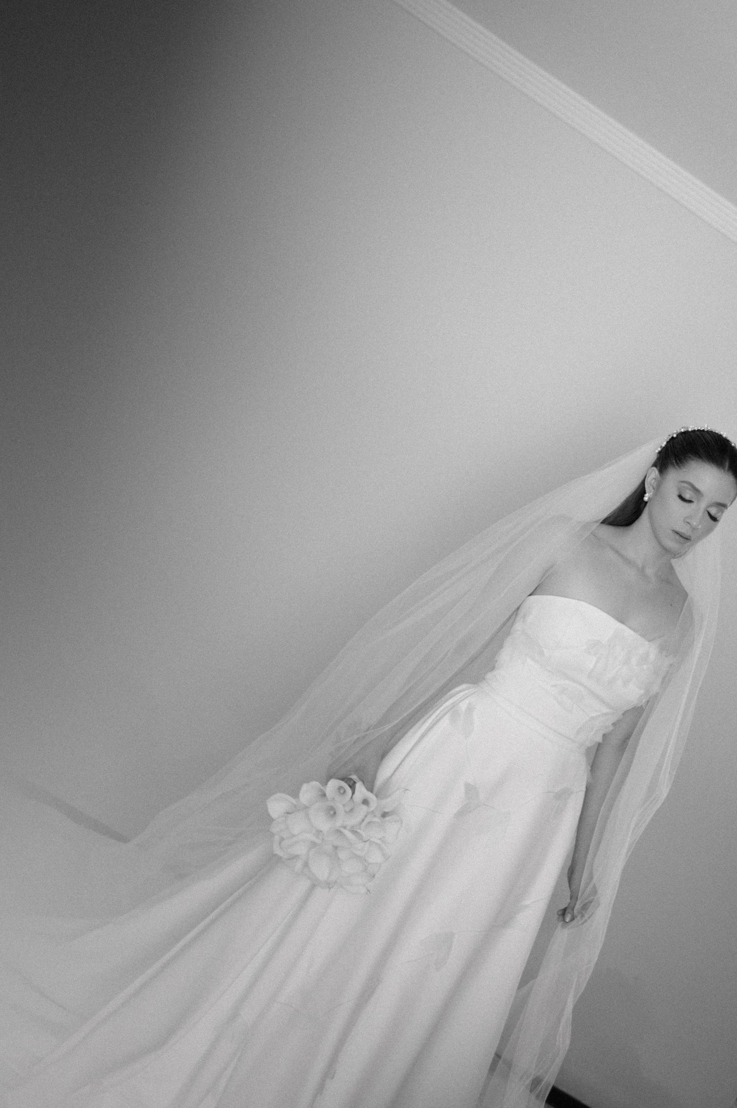 Full length black and white photo of bride in flowing wedding gown with veil.