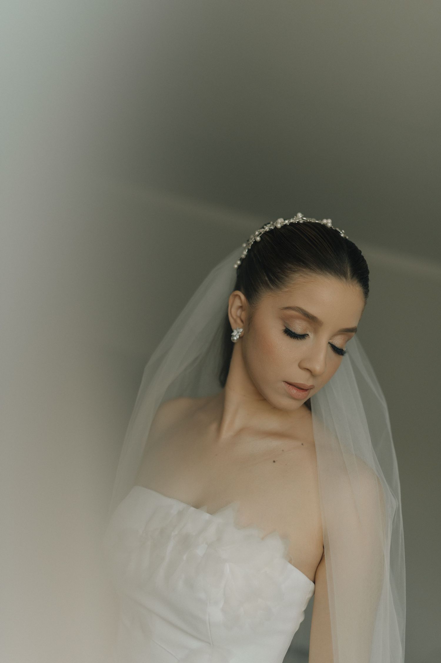 Soft focus bridal portrait with delicate veil and tiara against neutral background.