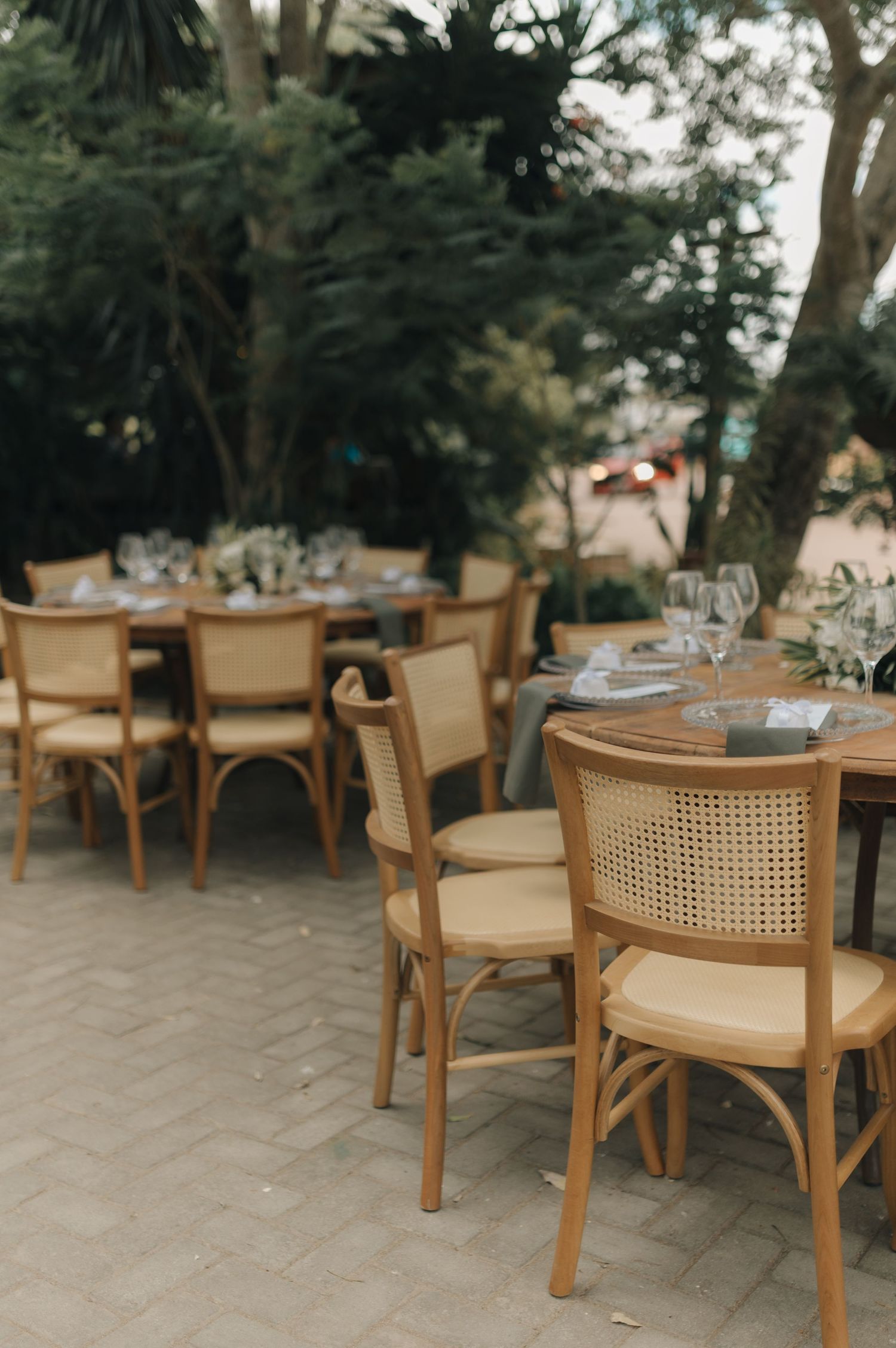 Outdoor wedding reception setup with wooden chairs and elegant table settings on a stone patio.
