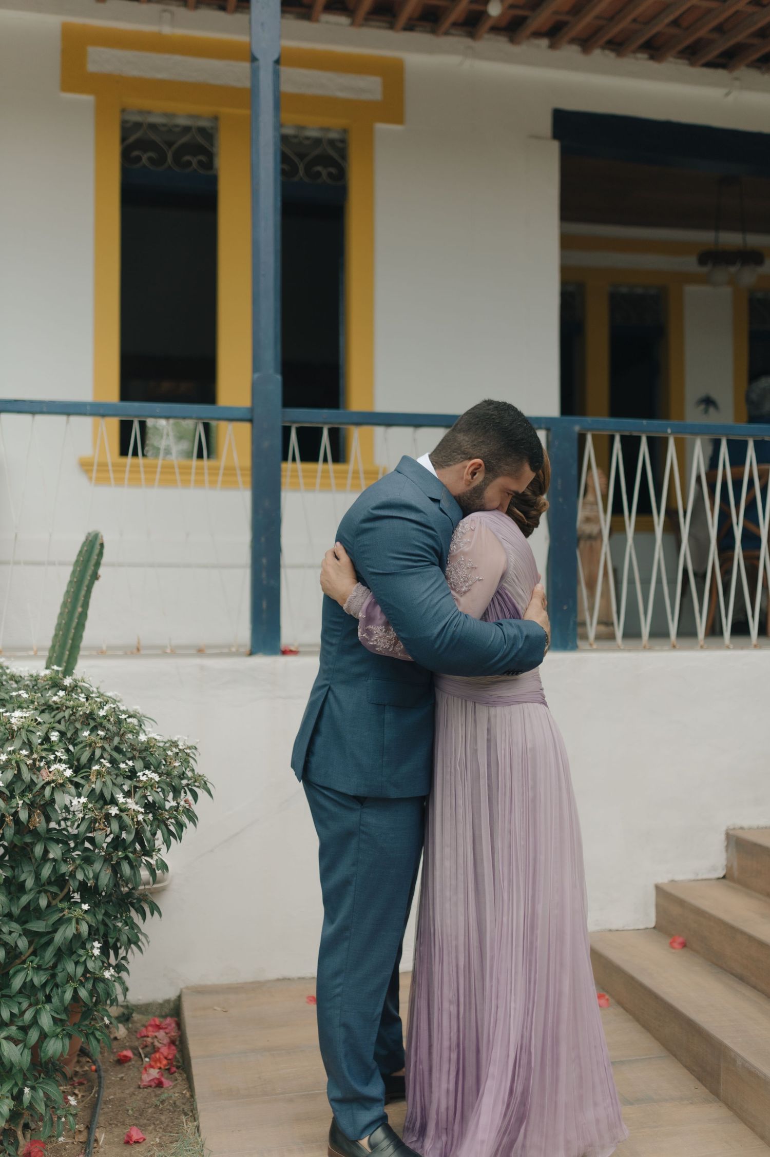 A tender moment between a couple in formal wear embracing on steps of a colonial-style building.