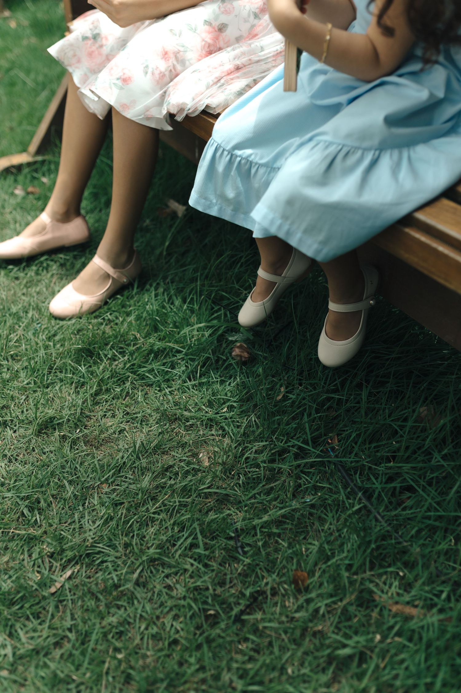 Two pairs of feet in dress shoes dangling from a bench over green grass.