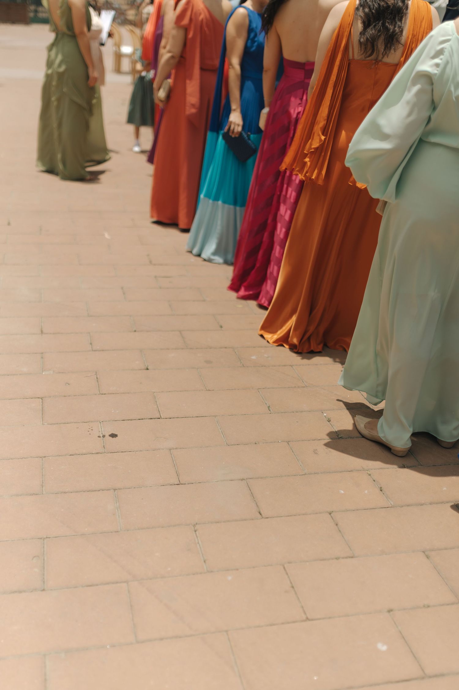A row of colorful formal dresses seen from behind on a tiled pathway.