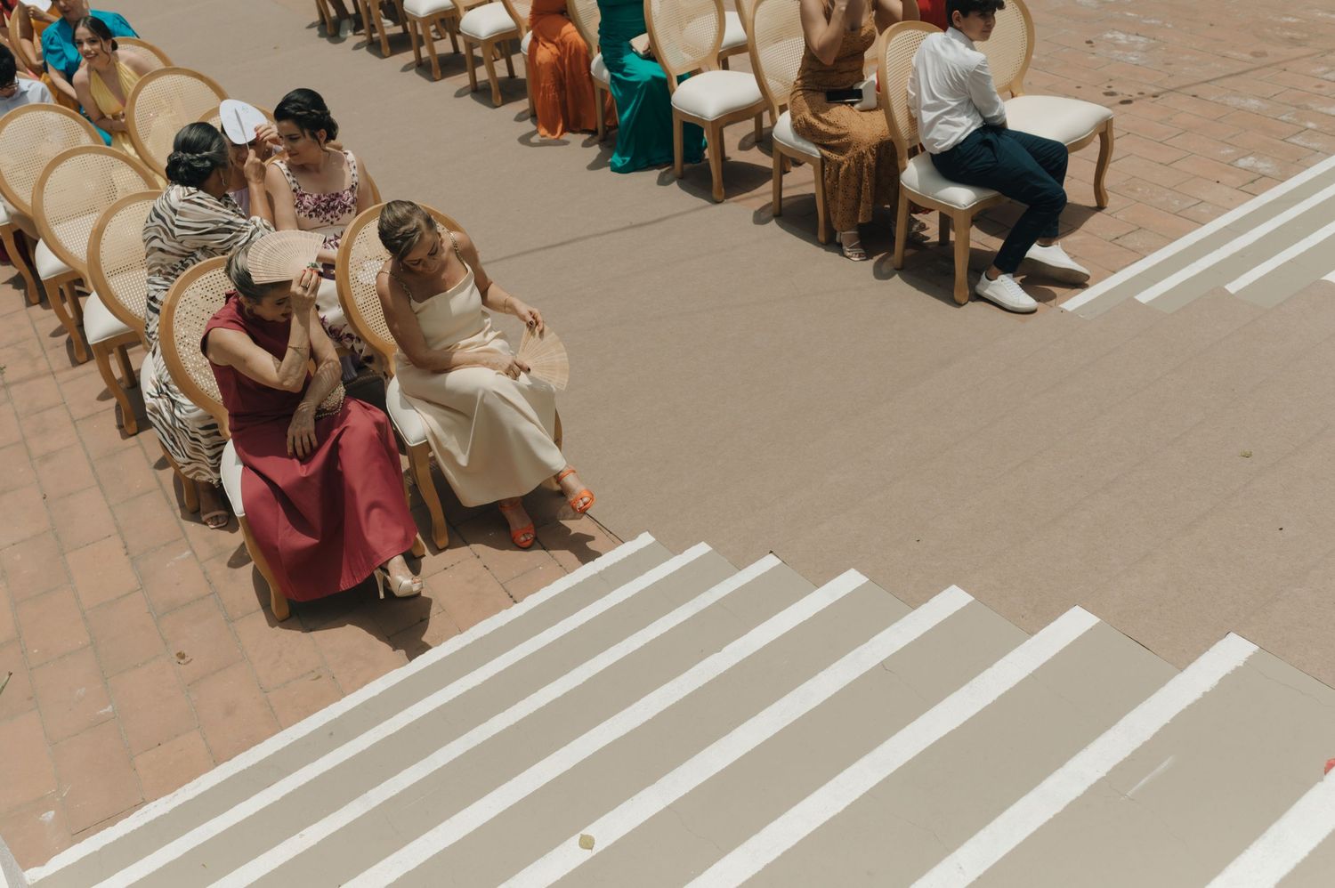 Wedding guests seated in rows with white lines painted on concrete ground.