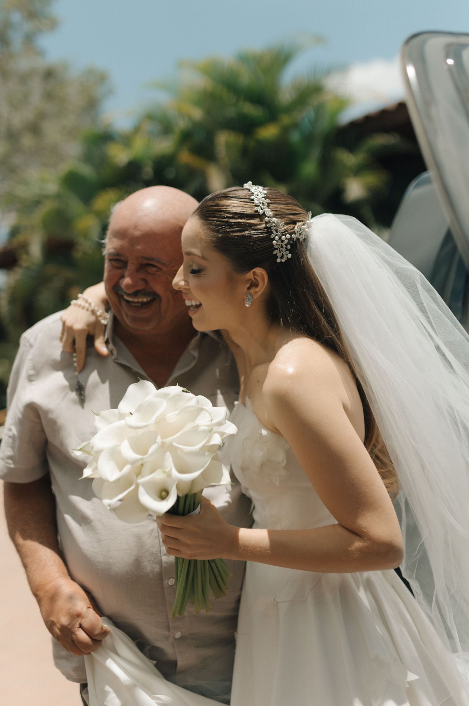 Candid outdoor wedding photo with white bouquet and flowing veil.
