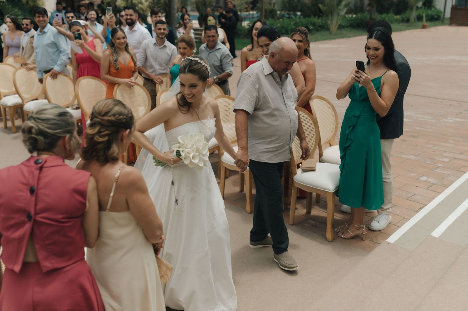 Outdoor wedding ceremony with guests seated on wooden chairs.