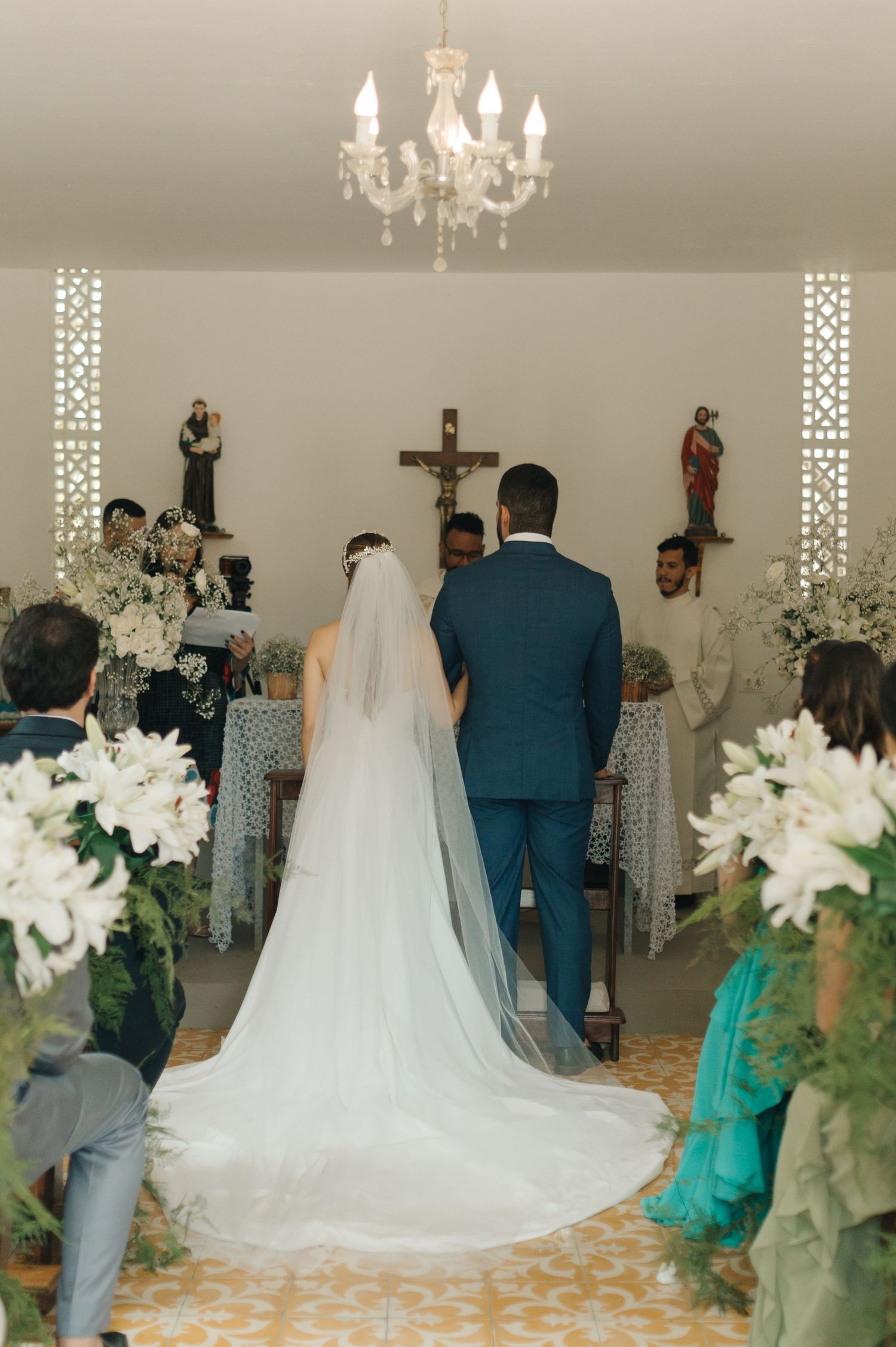 Wedding ceremony in white chapel with chandelier and floral decorations.