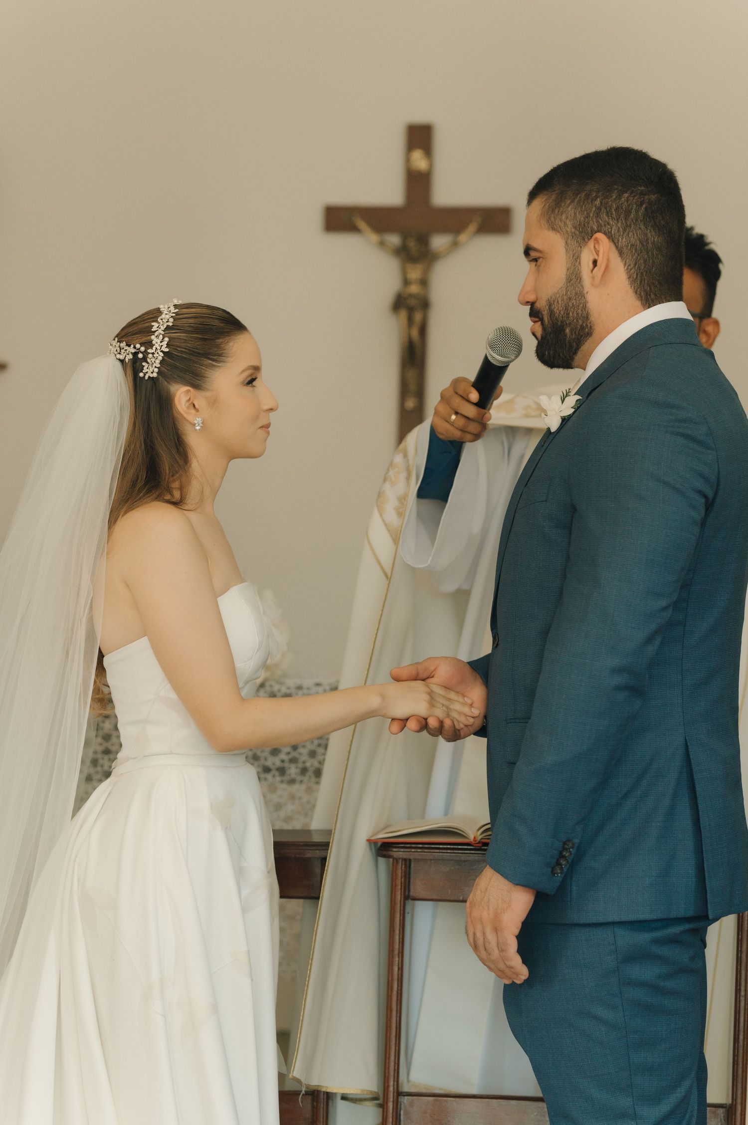 A bride and groom hold hands during their wedding ceremony in a Catholic church setting.