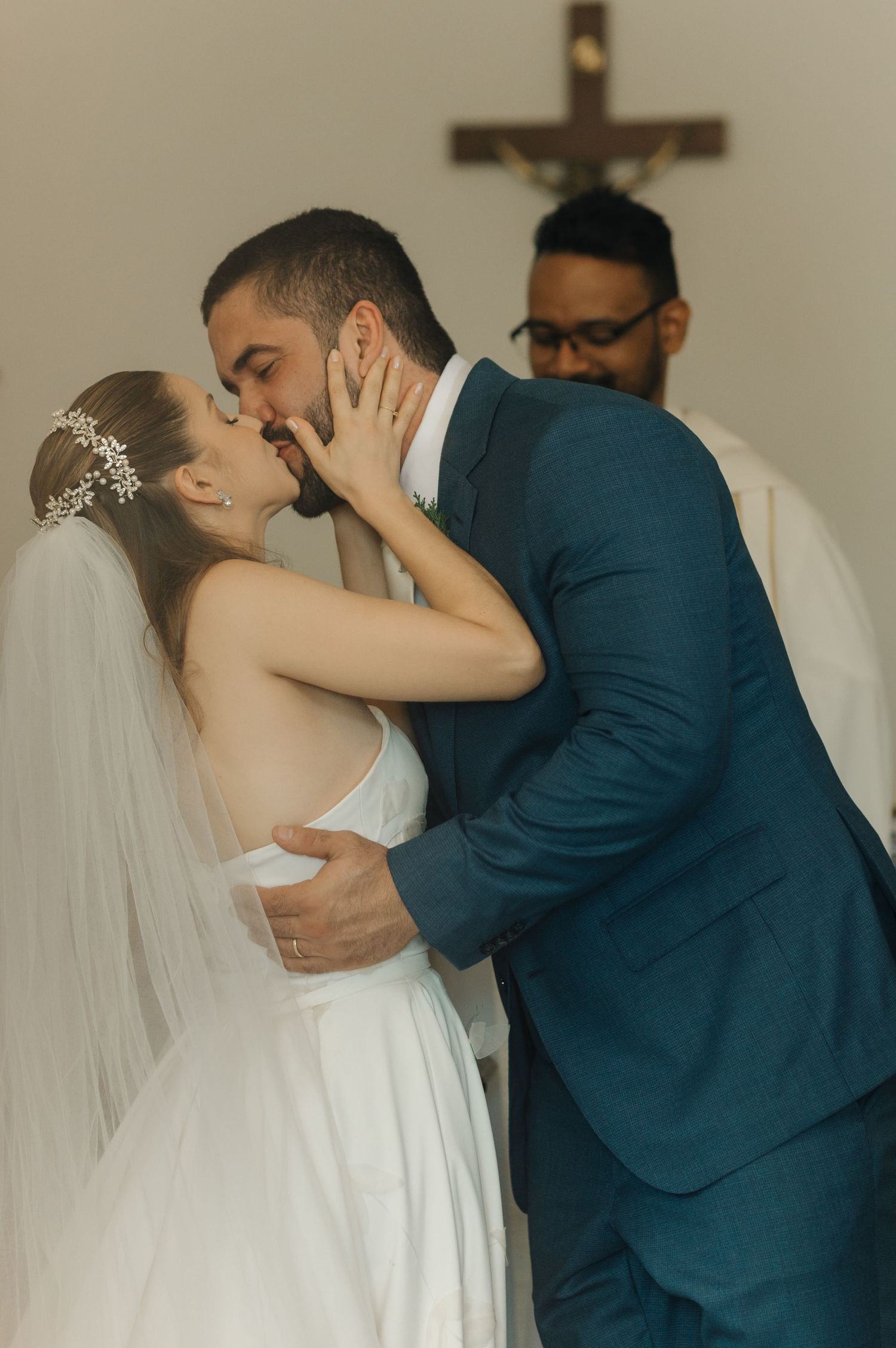 An intimate wedding ceremony moment capturing a couple's kiss beneath a hanging crucifix.