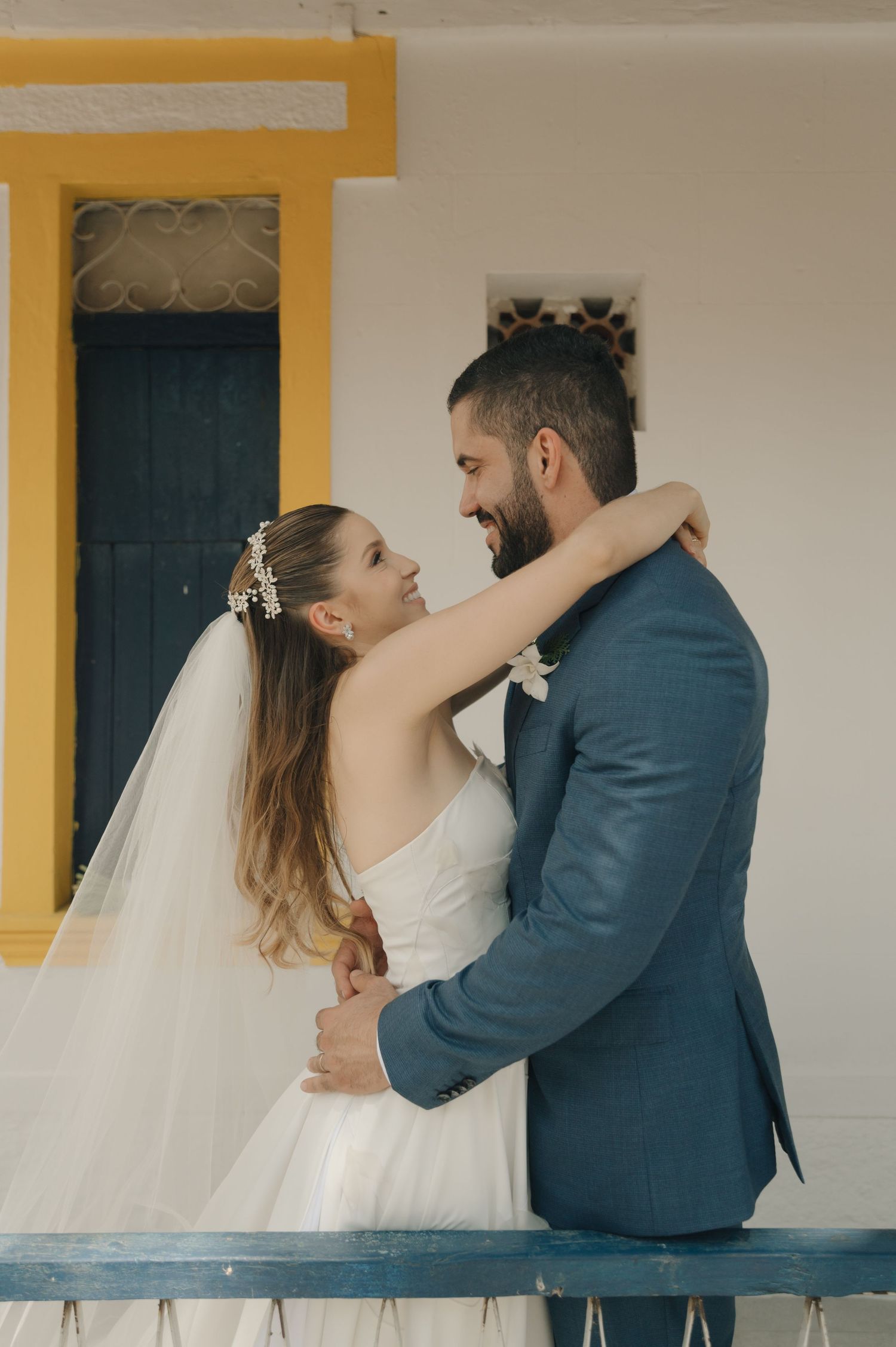 A romantic outdoor wedding portrait showing a couple embracing against a yellow and white colonial building.