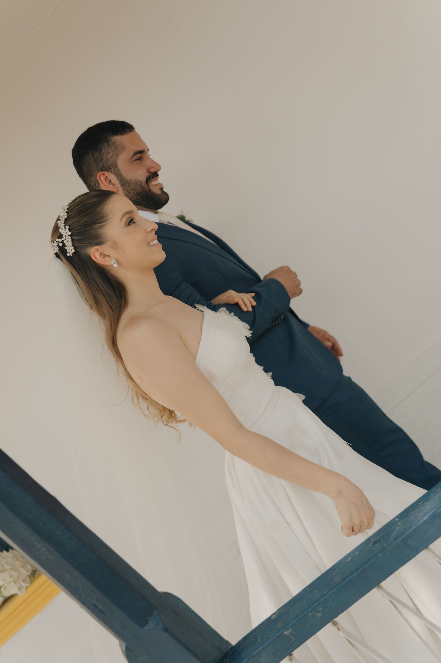 A playful wedding portrait showing a couple posing together on a blue-railed balcony.