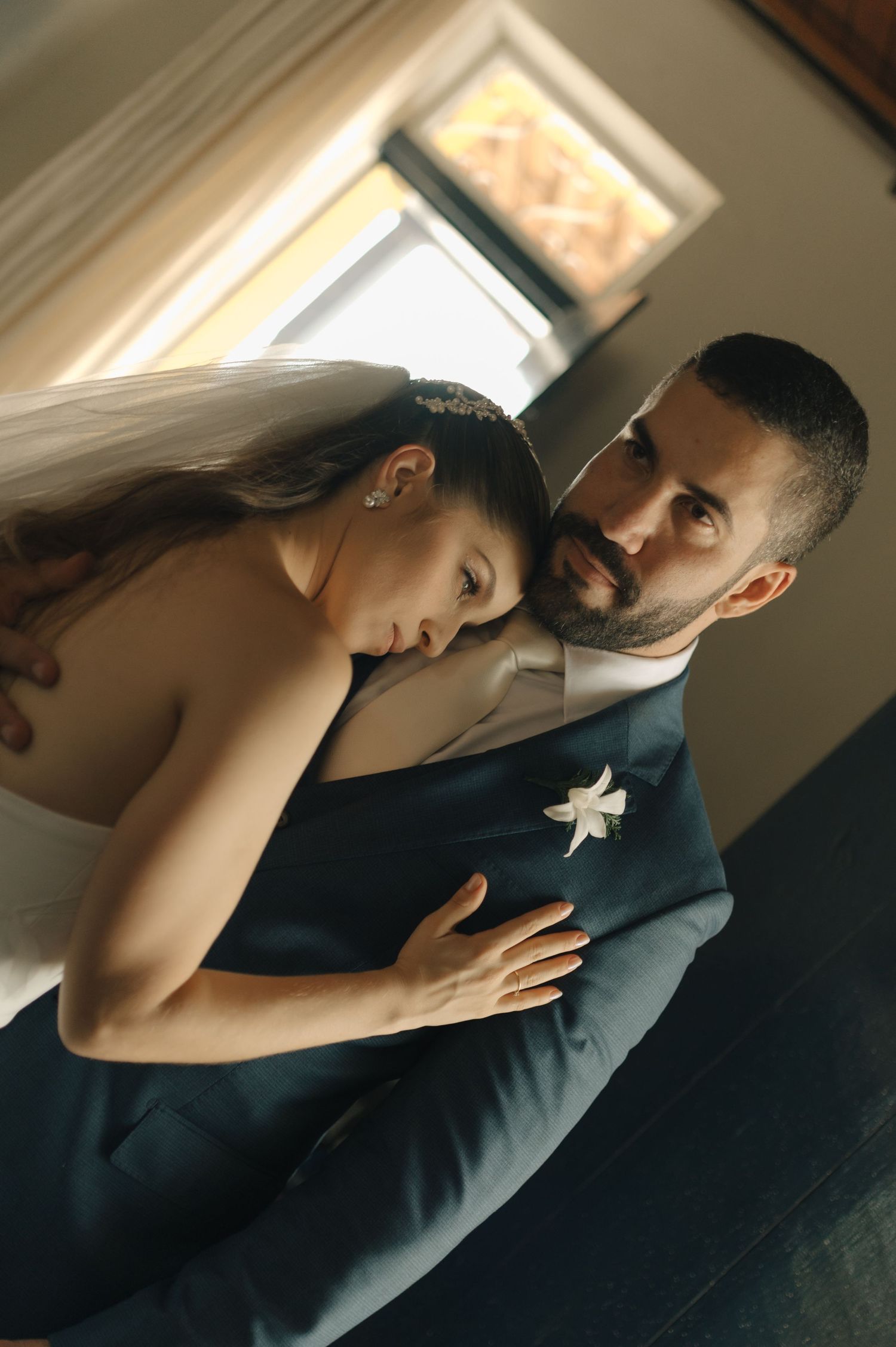 A moody wedding portrait capturing an intimate moment in dramatic window lighting.