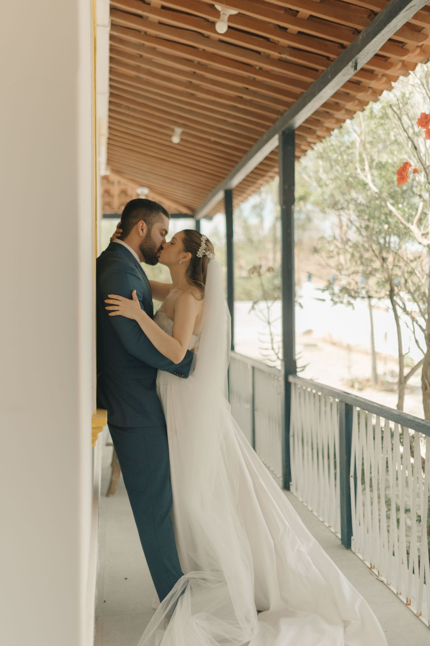 Romantic wedding couple sharing a loving moment on a sunlit veranda with flowing white veil.