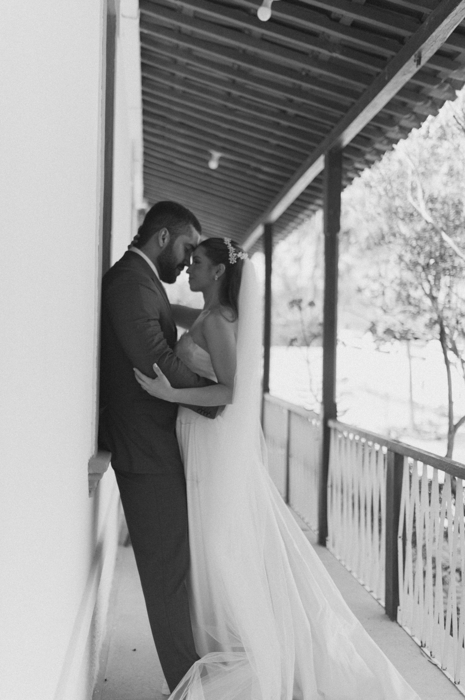 Intimate black and white portrait of newlyweds embracing against a wall on their wedding day.