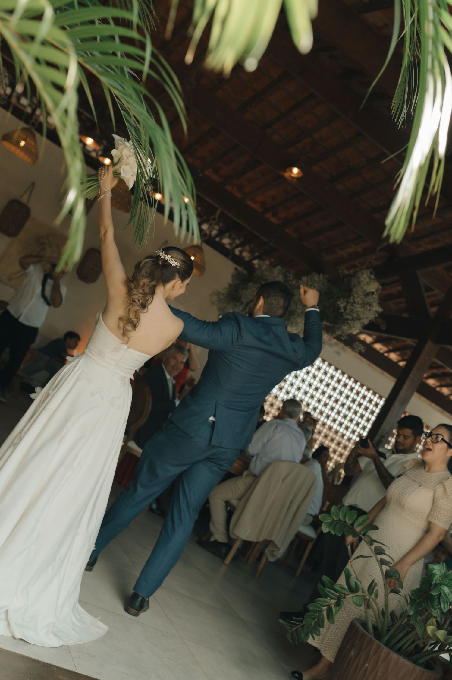 Newlyweds performing their first dance under palm fronds at an indoor wedding reception.