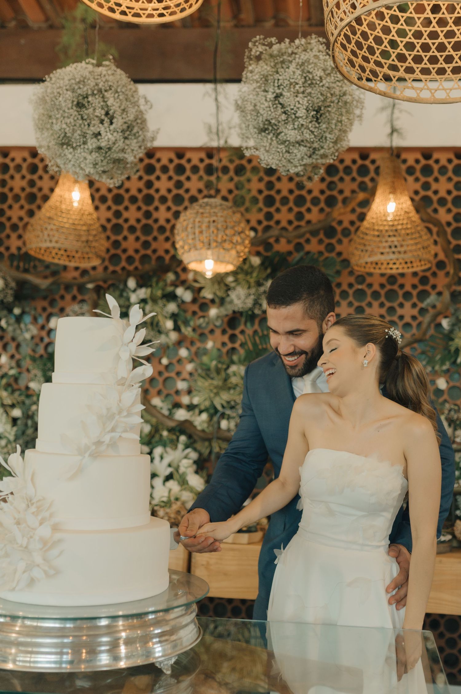 Happy couple cutting their elegant white wedding cake under decorative hanging lights.